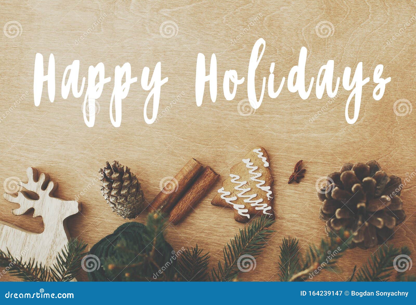 happy holidays text sign on stylish rustic frame of pine branches, cones, gingerbread cookies,thread, cinnamon, anise on rural