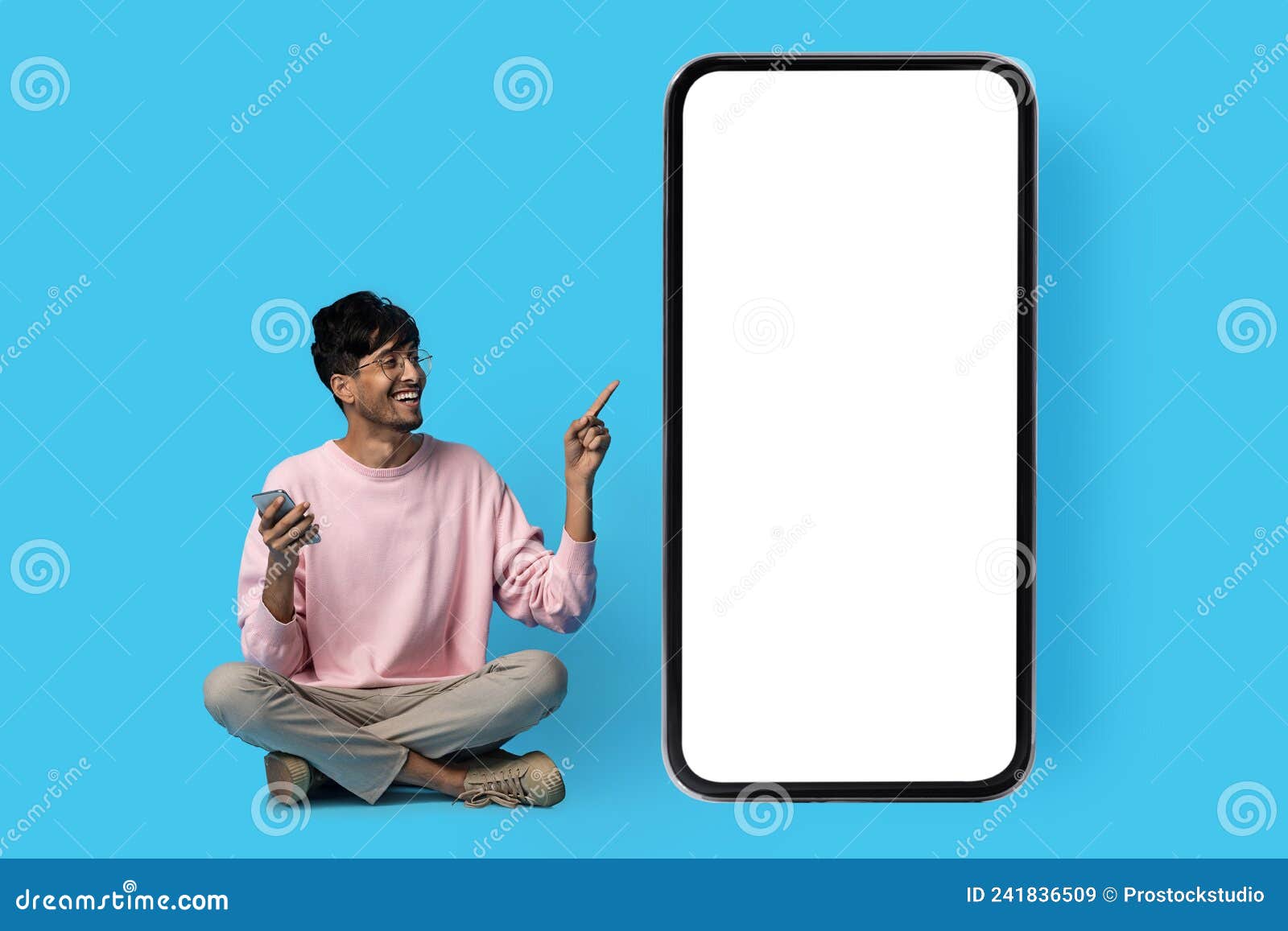 happy indian guy pointing at huge smartphone with blank screen