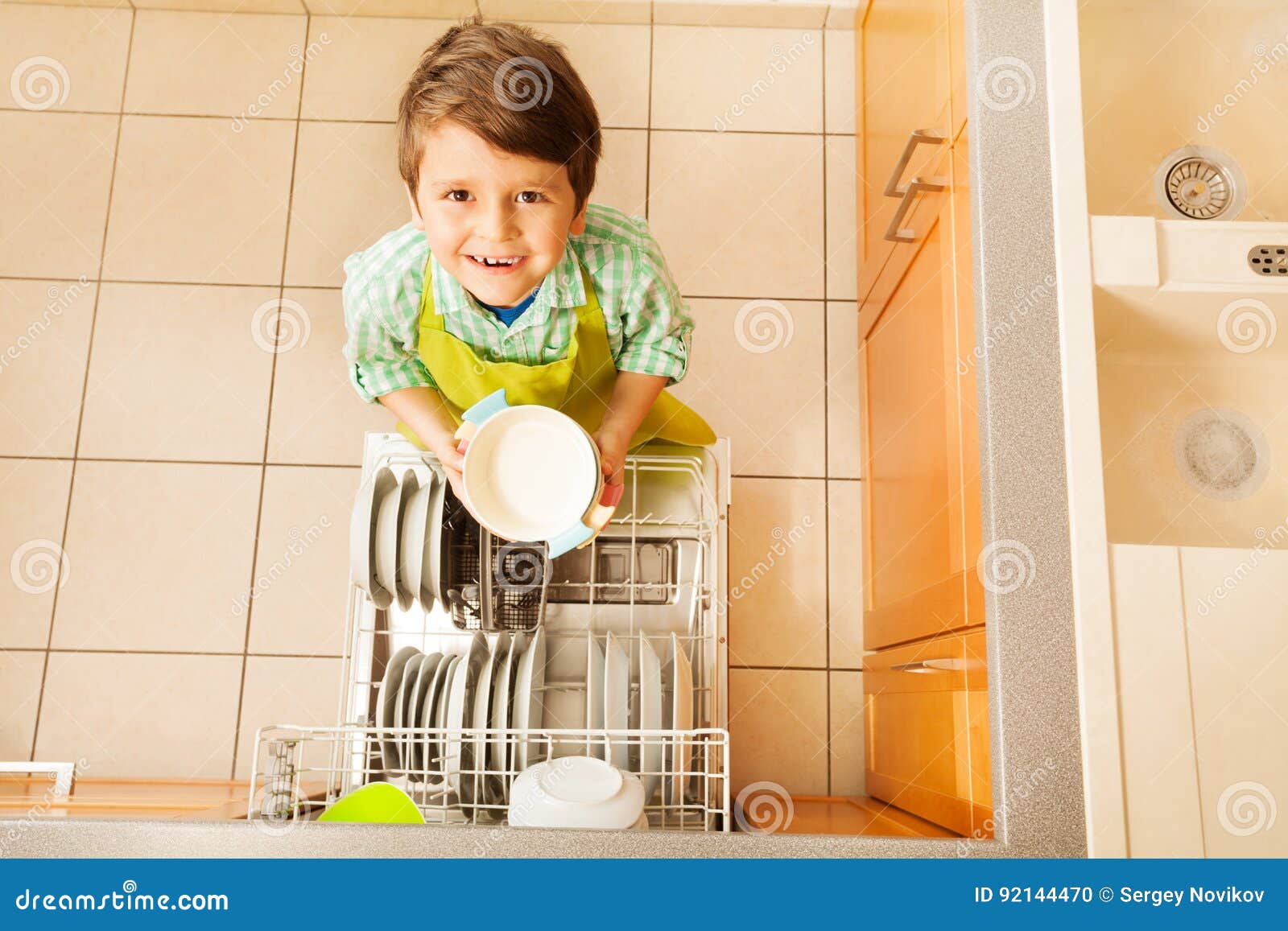 happy kid boy taking out dishes from dishwasher