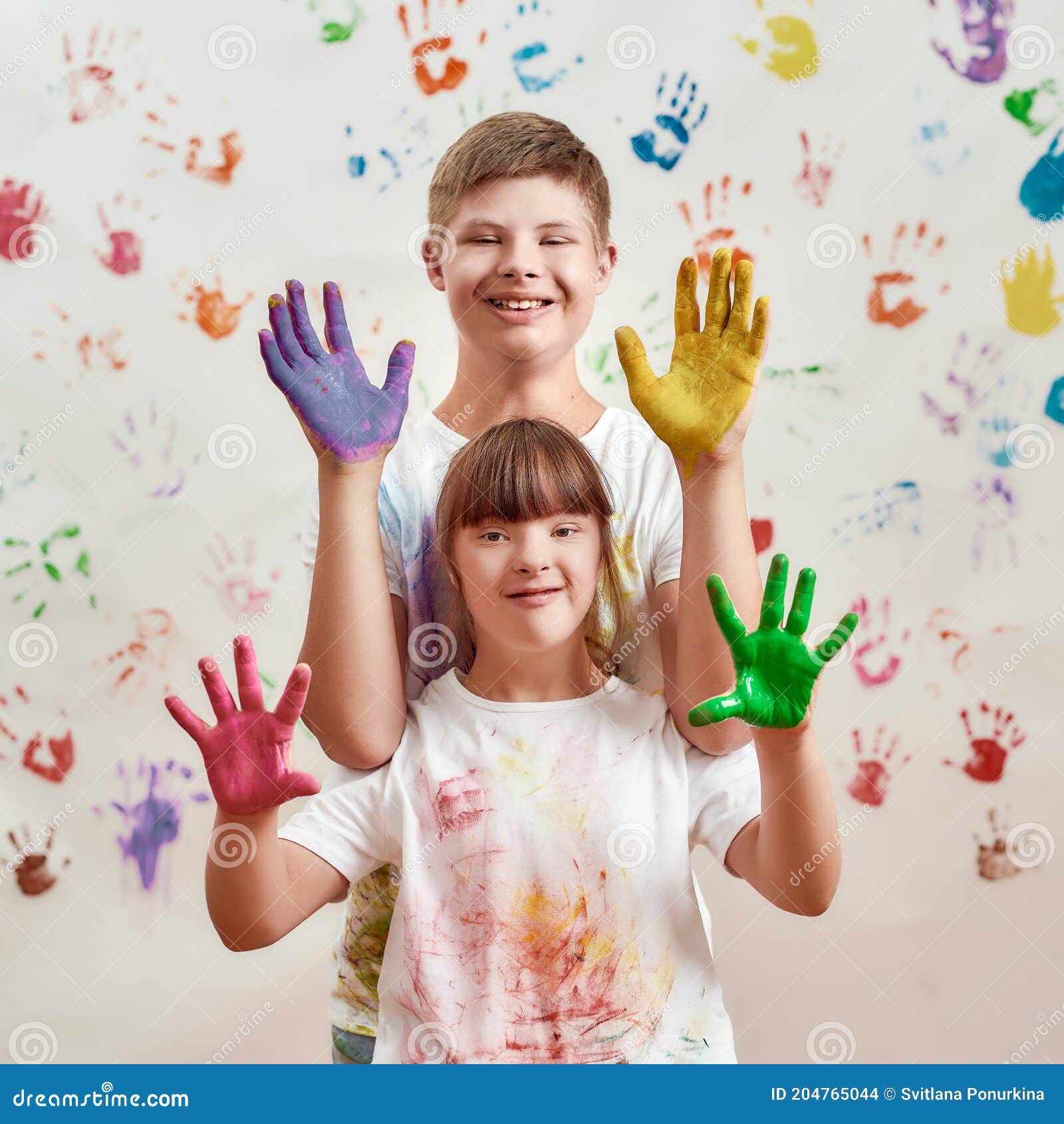 happy kids, disabled boy and girl with down syndrome smiling at camera, showing their hands painted in colorful paints