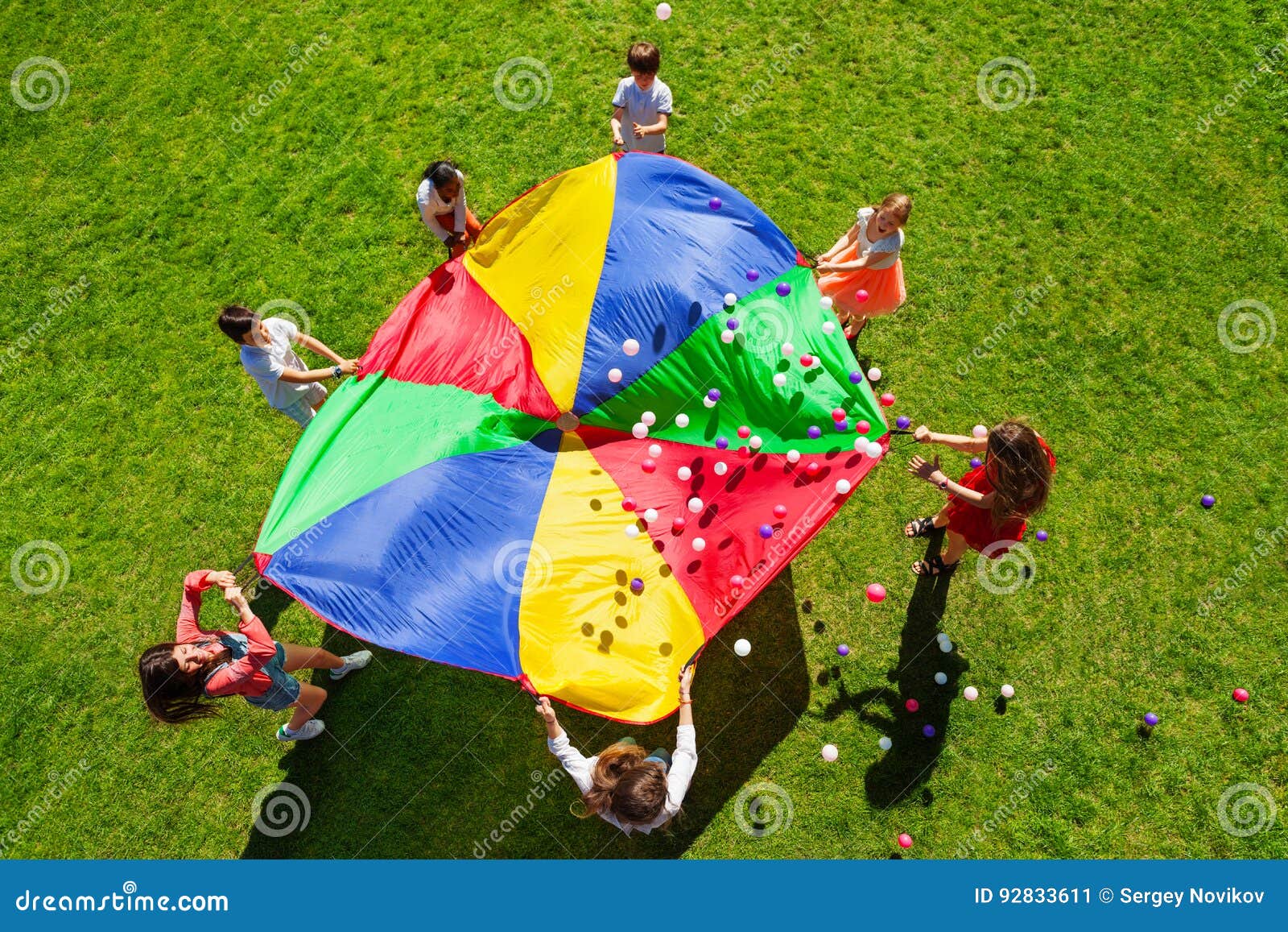 happy kids waving rainbow parachute full of balls