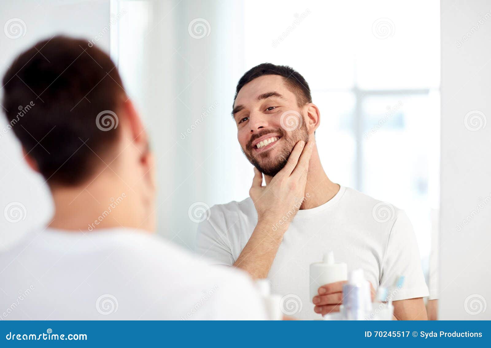happy man applying aftershave at bathroom mirror