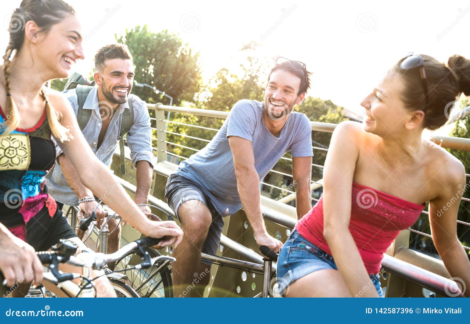 happy millenial friends having fun riding bicycle in city park - friendship concept with young millennial people students biking