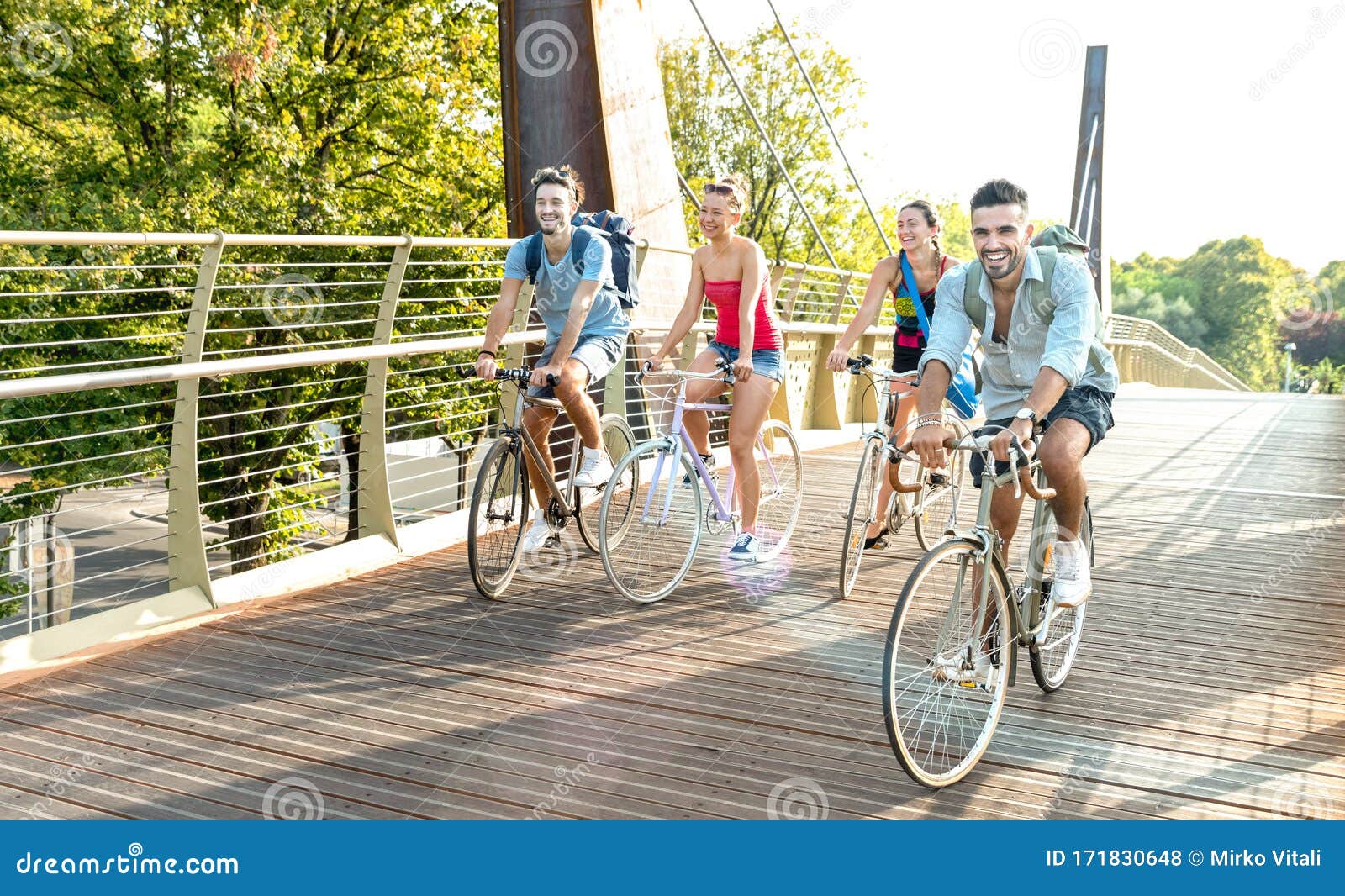 happy millenial friends having fun riding bike at city park - friendship concept with young millennial students biking together