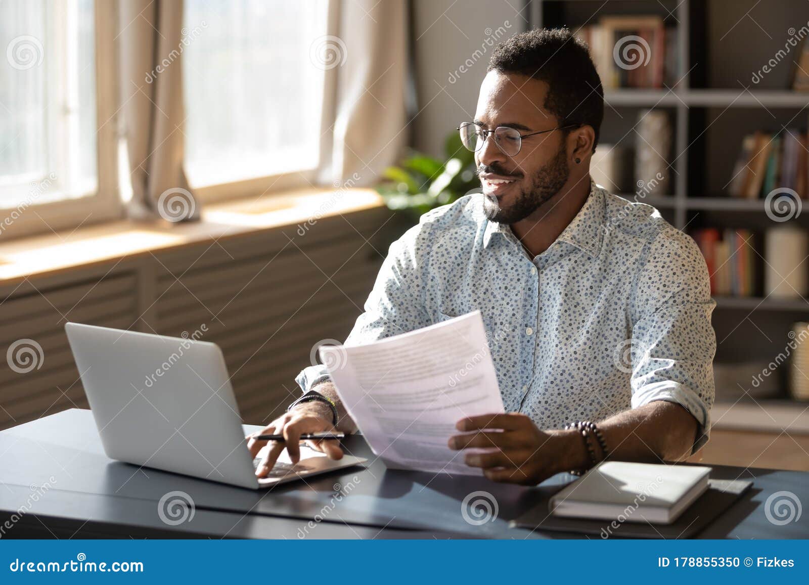 happy millennial african american businessman in eyewear doing paperwork.