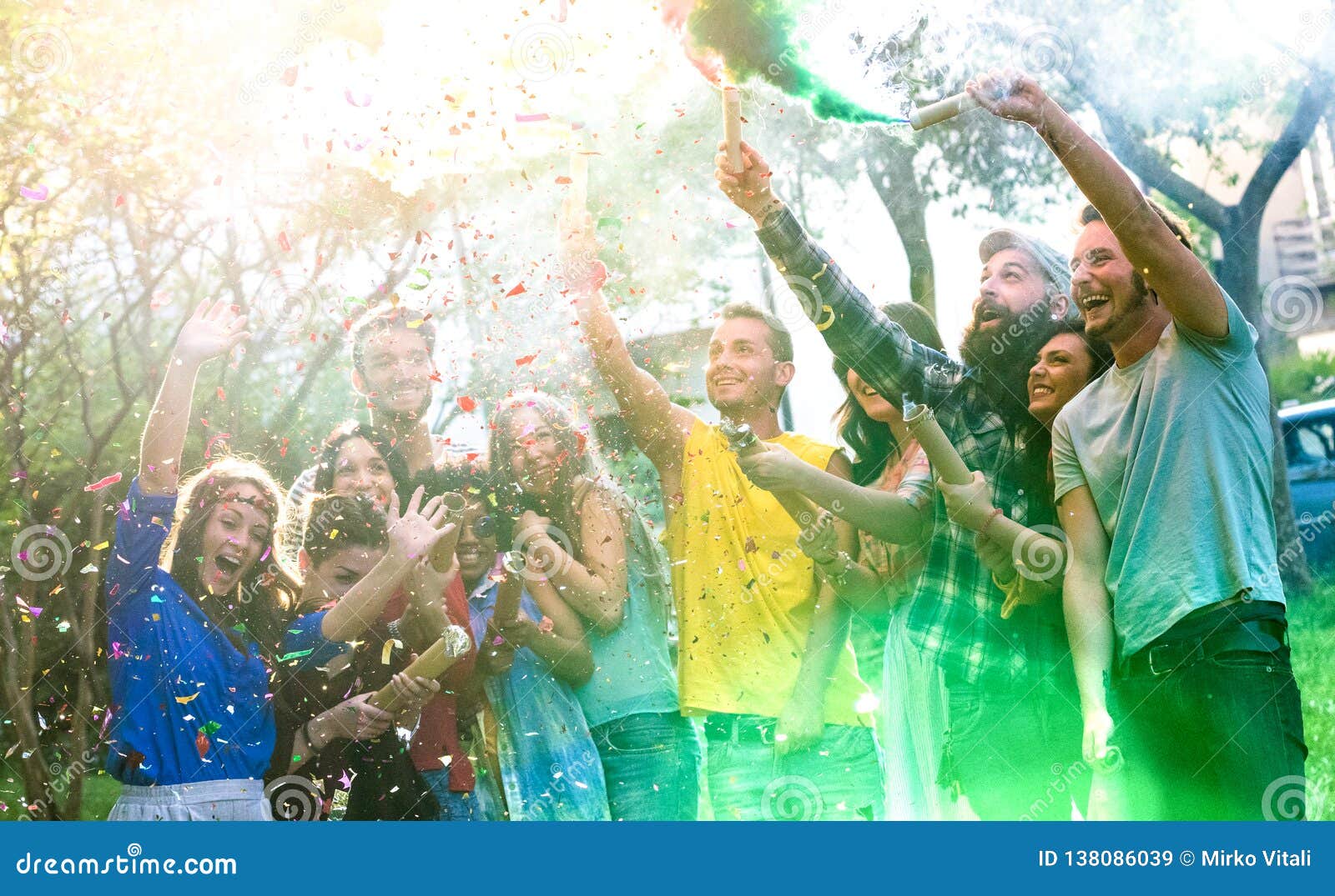 happy millennial friends having fun at garden party with multicolored smoke bombs outside - young millenial students celebrating