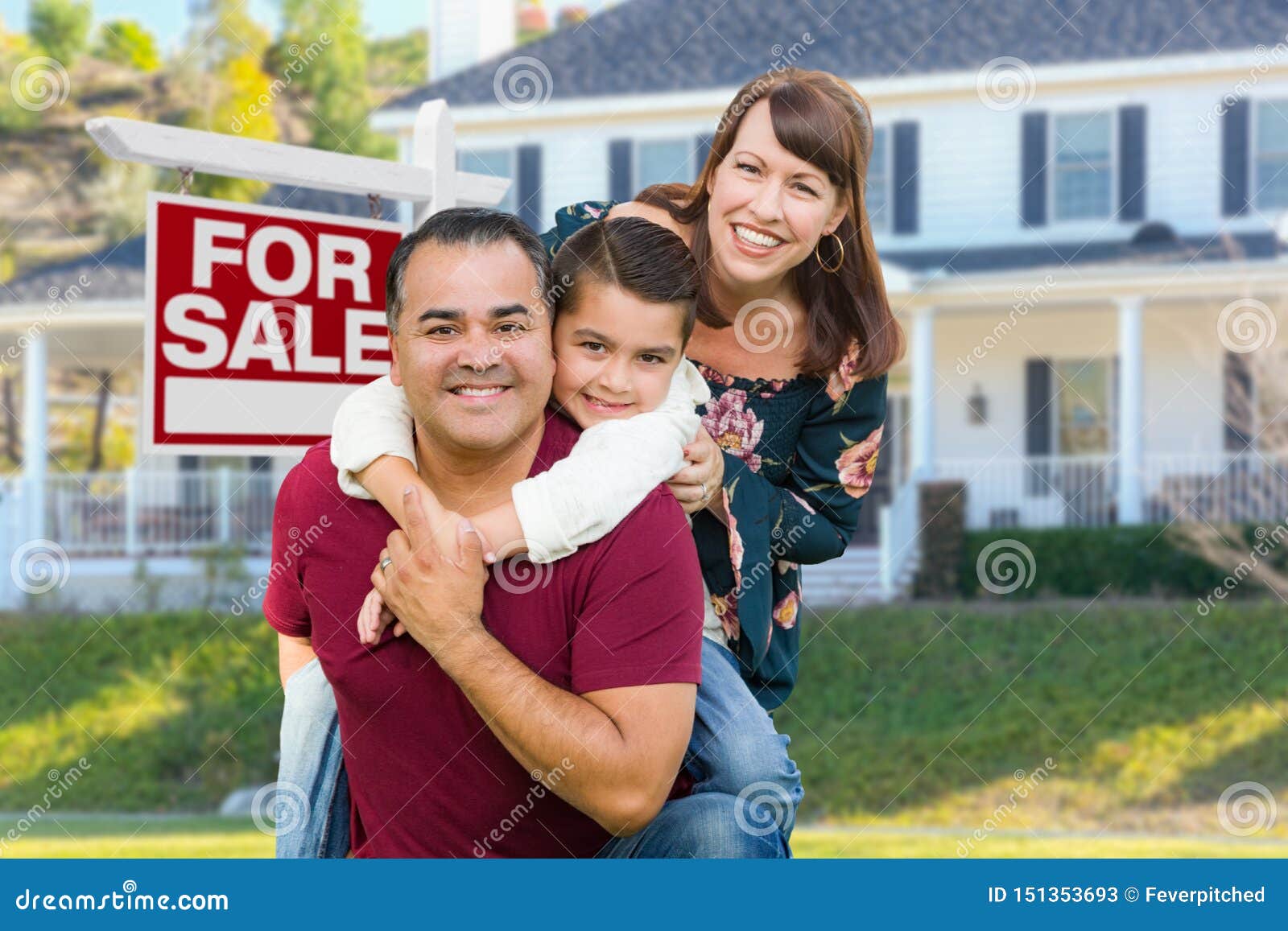 happy mixed race family in front of house and for sale real estate sign