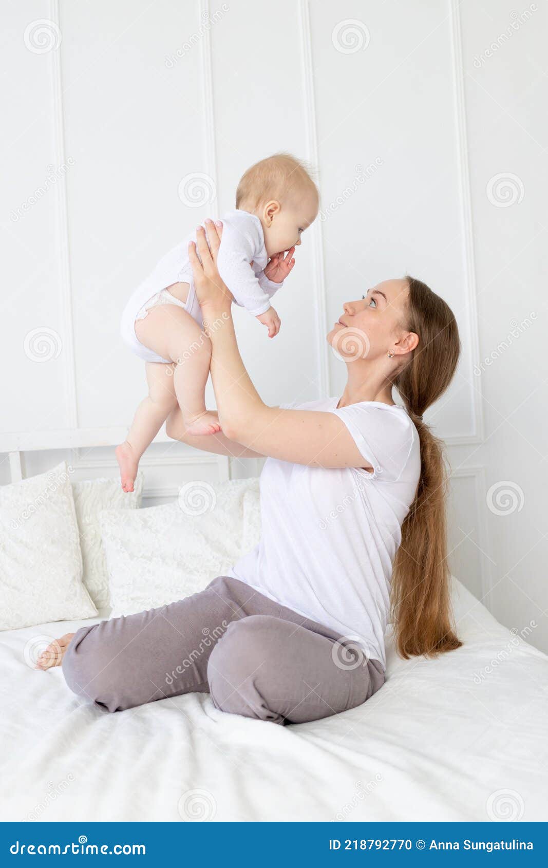 Happy Mom Holds a Baby in Her Arms Lifting it Up on the Bed at Home ...