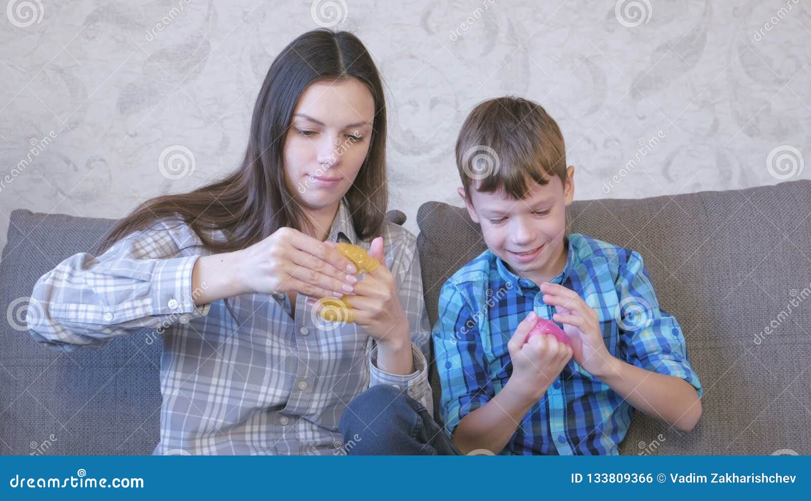 Happy Mom And Son Are Playing With Slime Sitting On The Sofa Stock