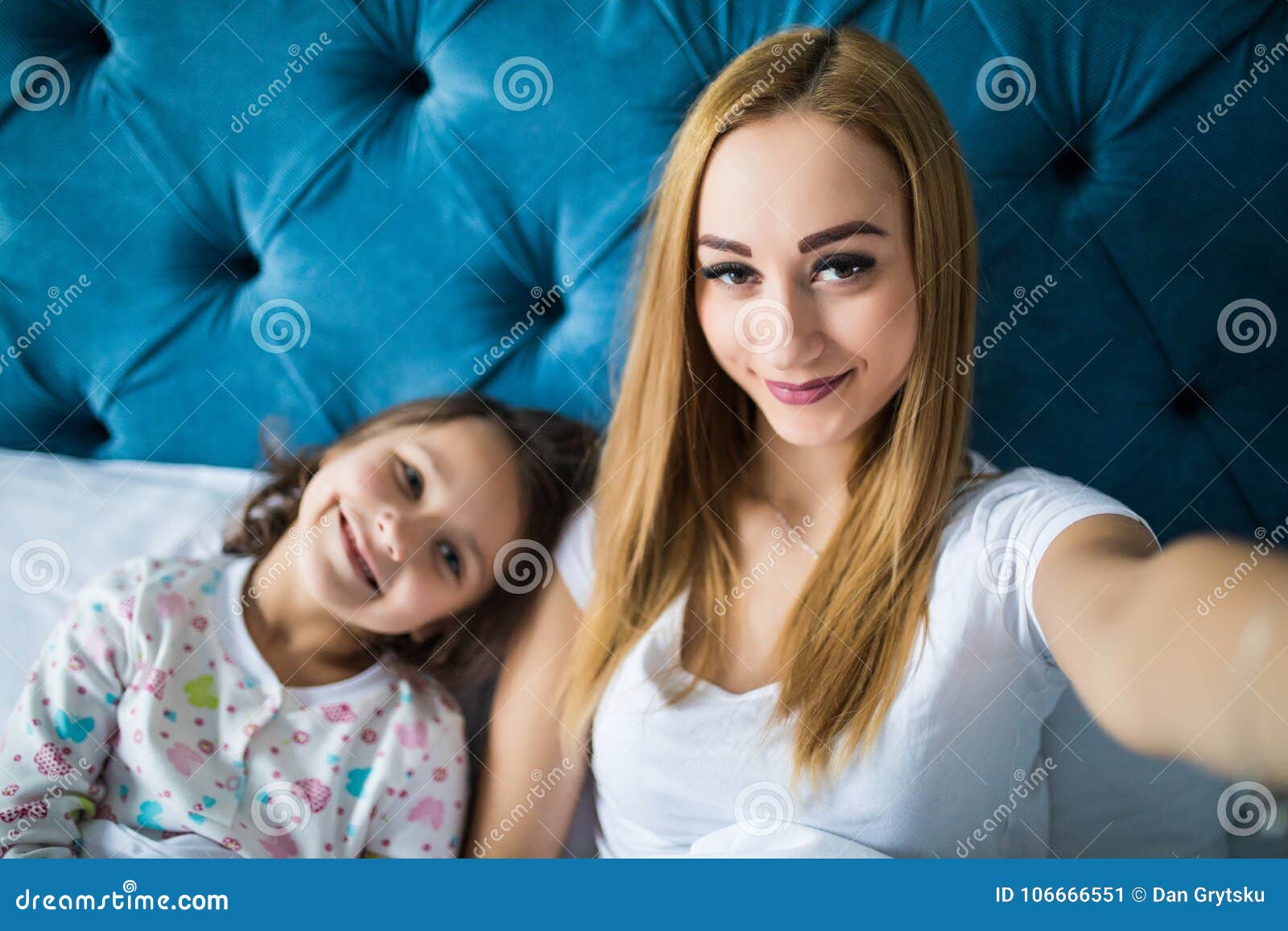 happy mother and daughter in pajamas taking selfie with smartphone on bed