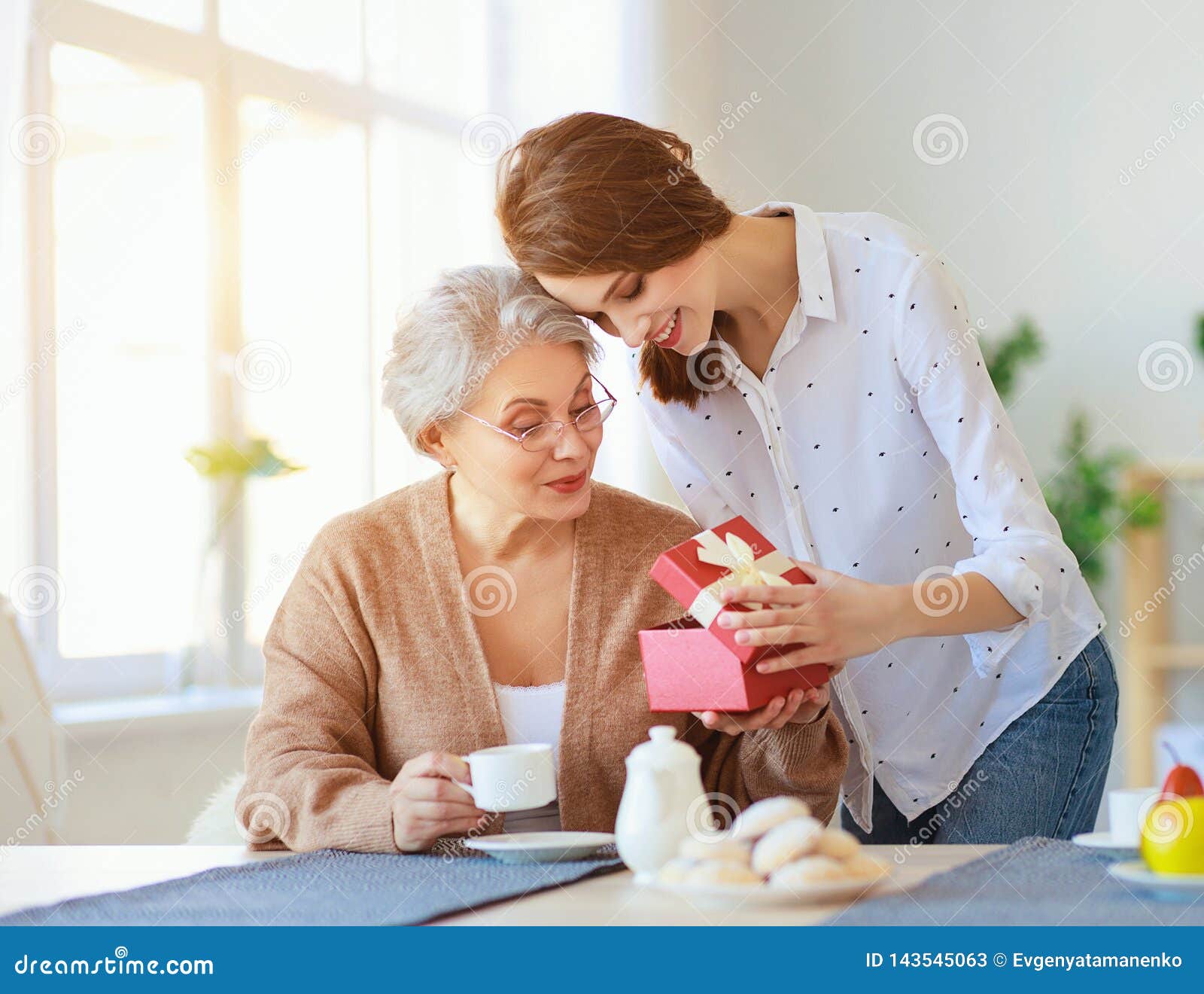happy mother`s day! adult daughter gives gift  and congratulates an elderly mother on holiday
