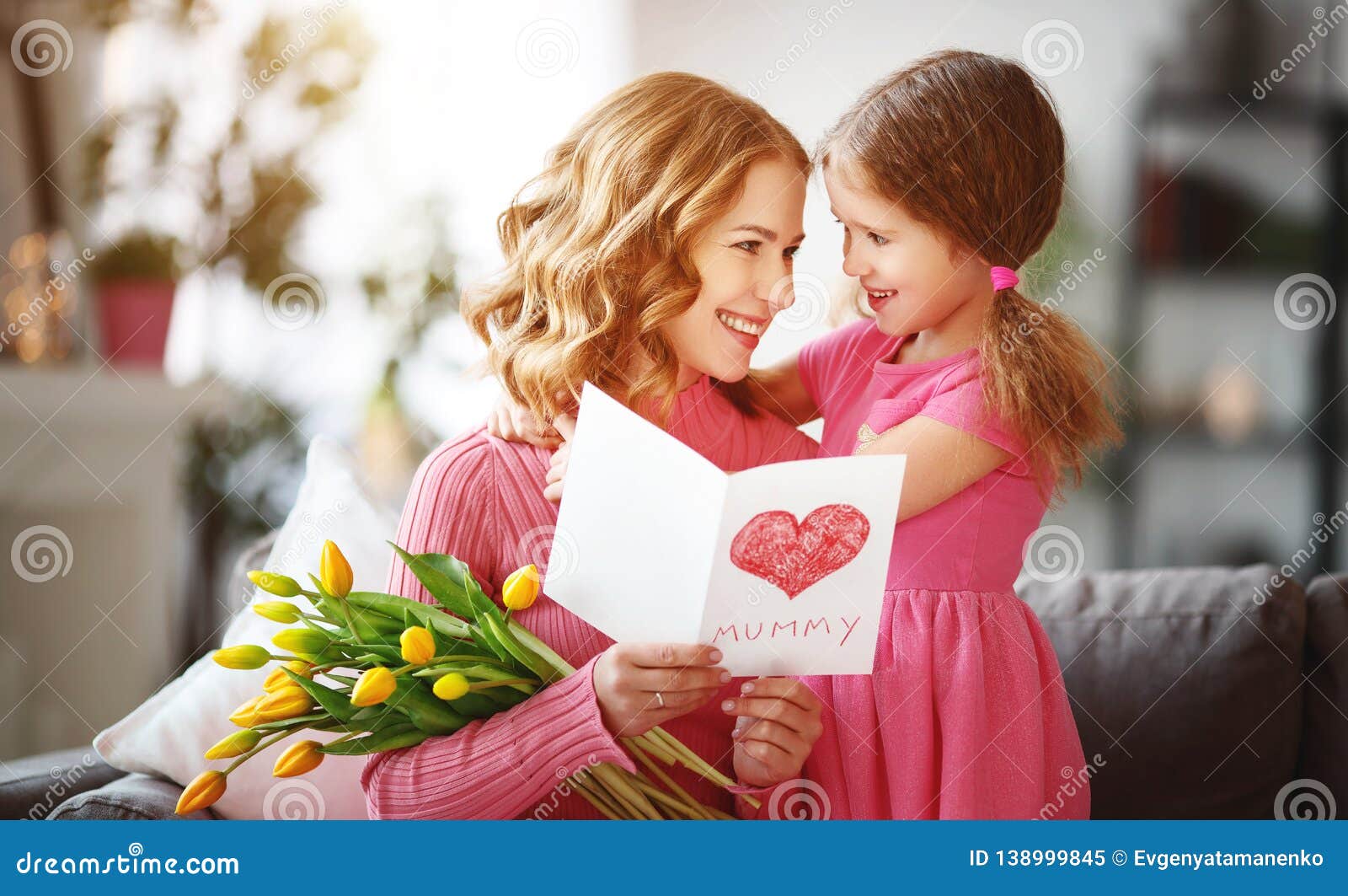 happy mother`s day! child daughter gives mother a bouquet of flowers to tulips and postcard