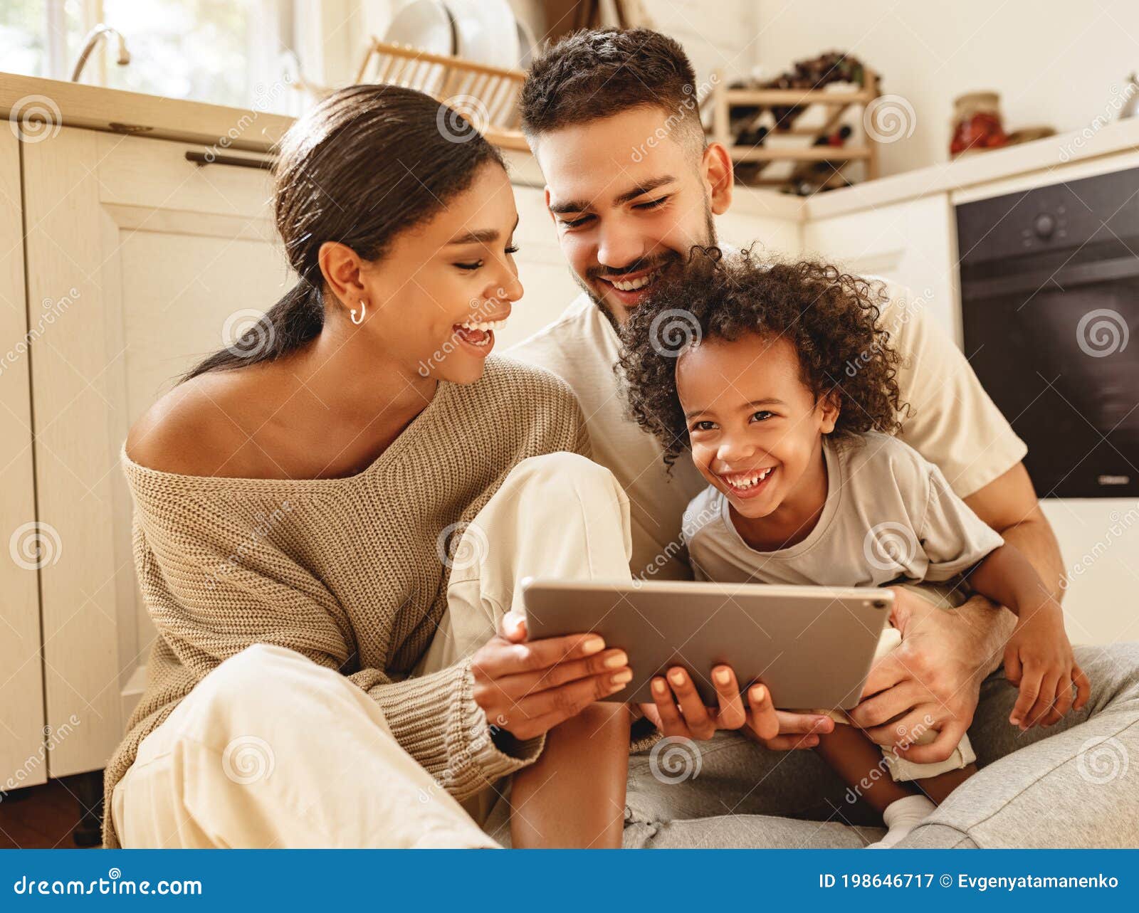 happy multi ethnic family: parents and son laughed and watch funny video on a tablet  at home