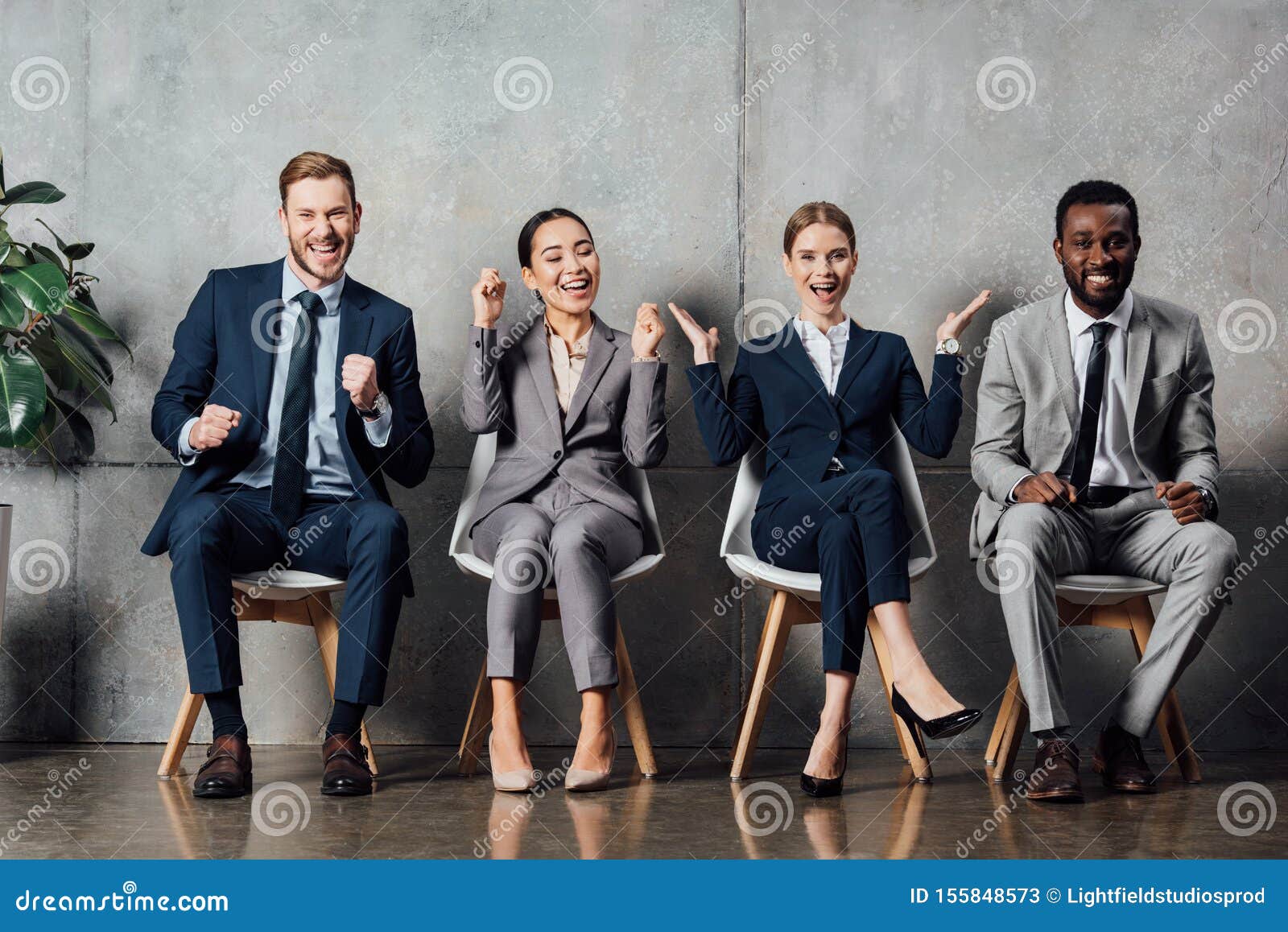 happy multiethnic businesspeople sitting on chairs and cheering with clenched fists in