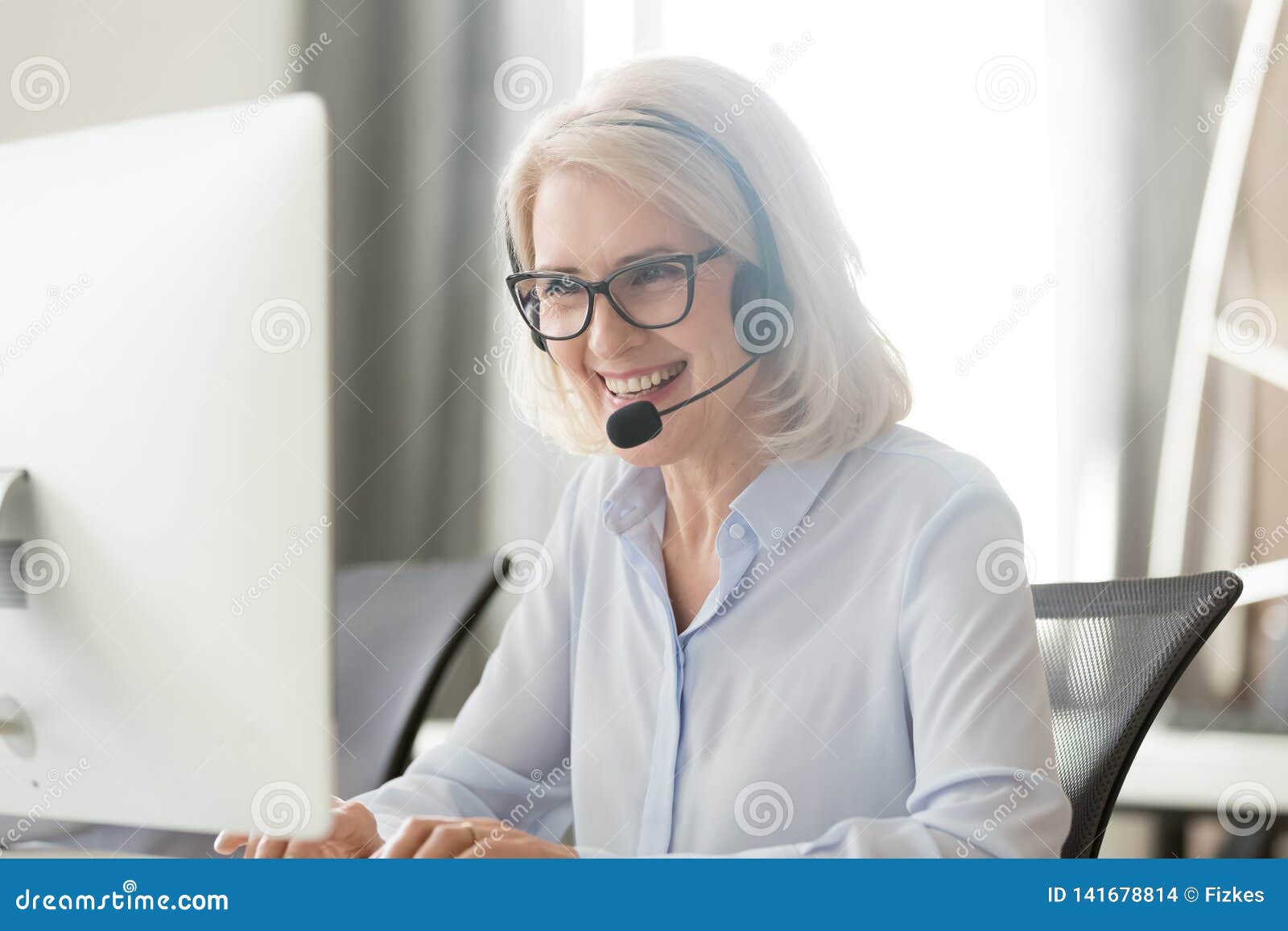 happy old businesswoman in headset making call looking at computer