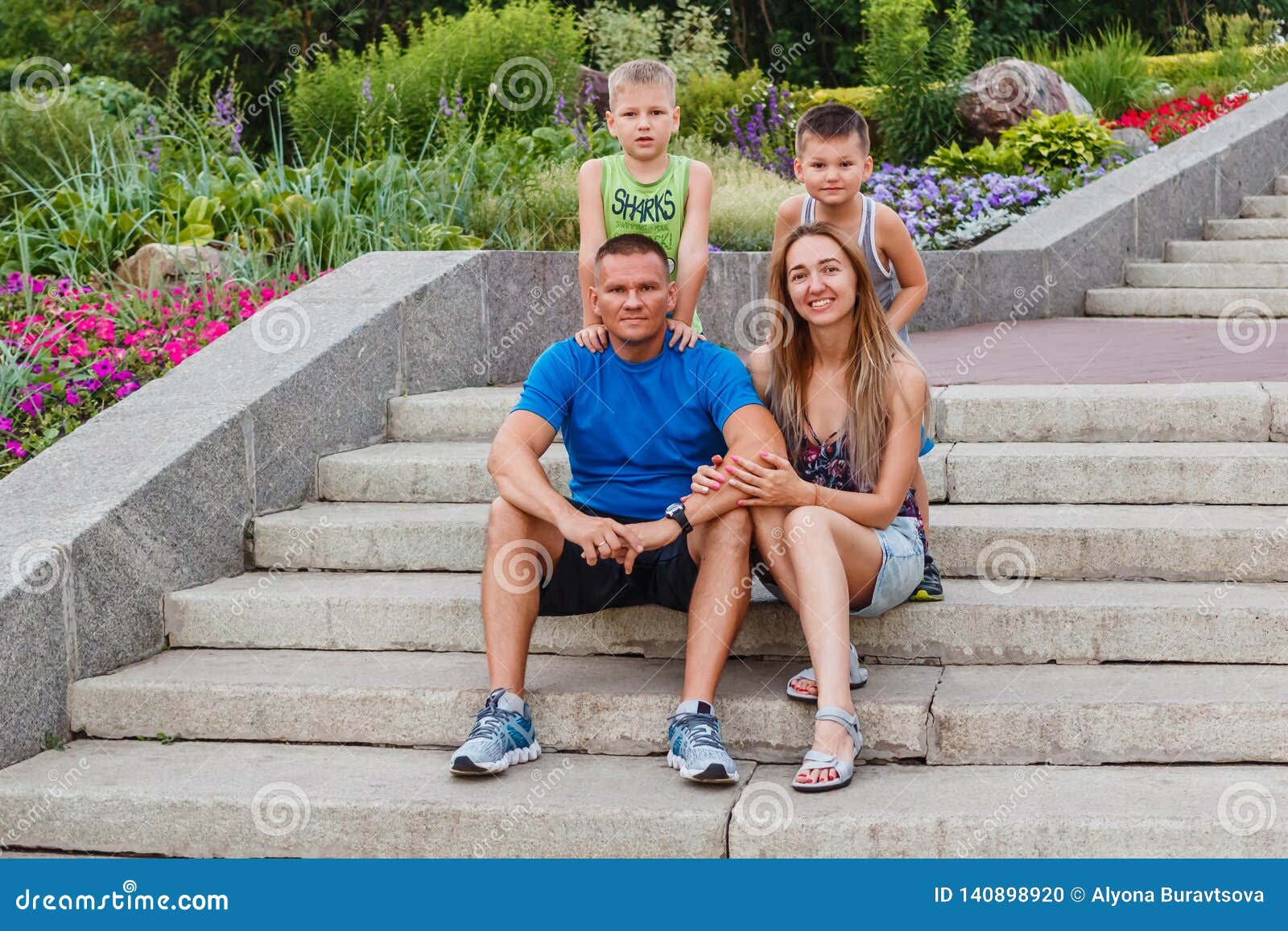 Happy Parents And Two Sons In The Summer On The Steps In The Park