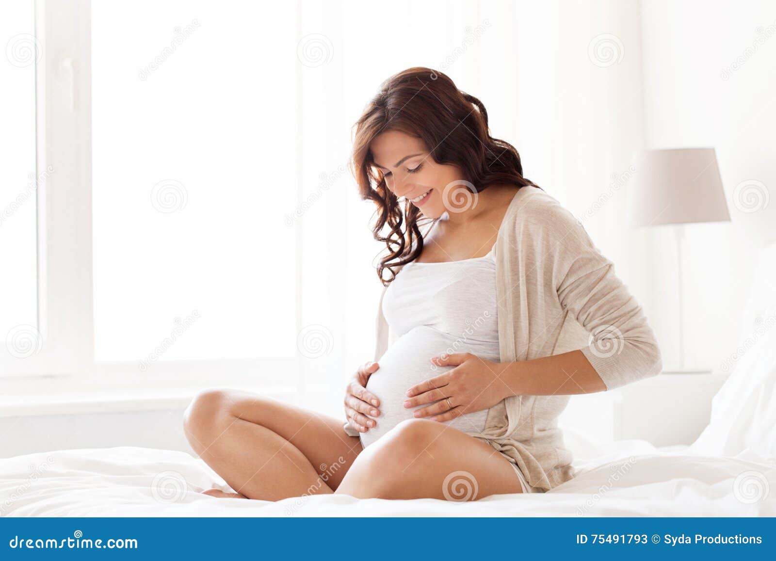 happy pregnant woman sitting on bed at home