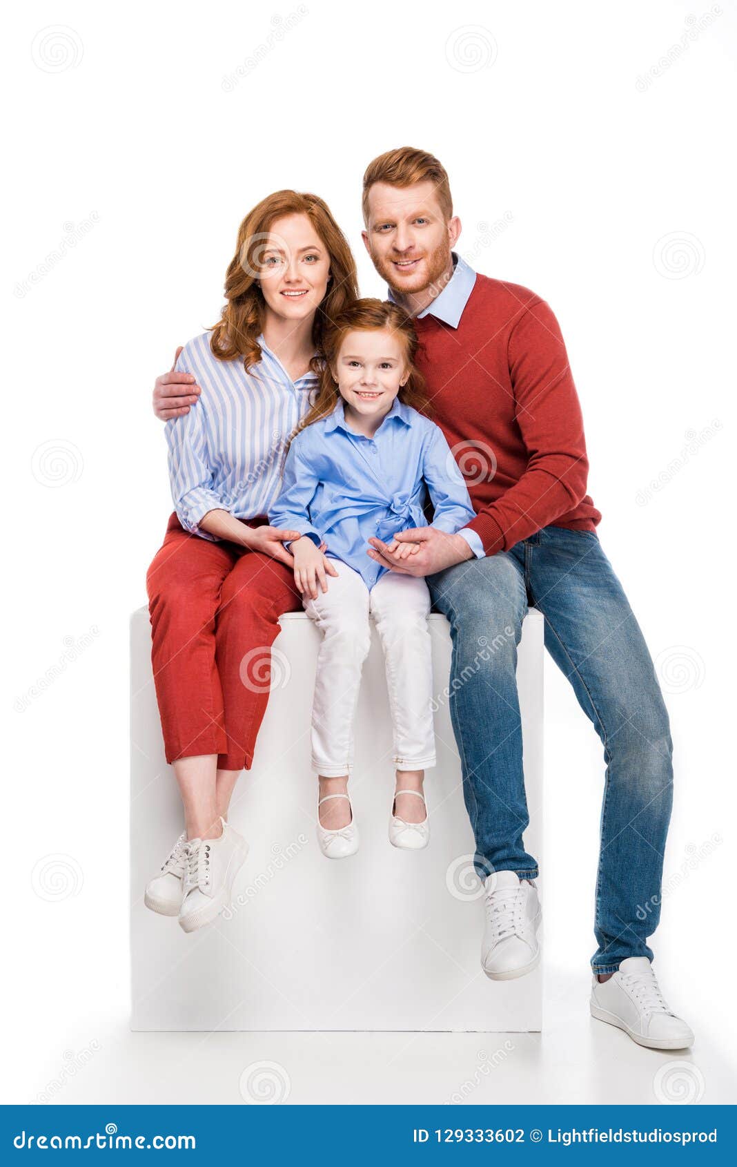 happy redhead family sitting on white cube and smiling at camera