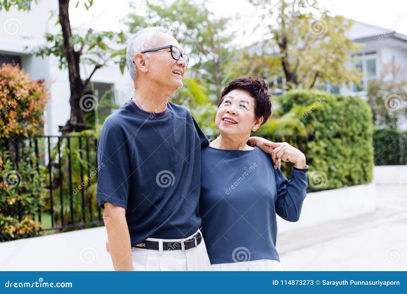 happy retired senior asian couple walking and looking at each other with romance in outdoor park and house in background.