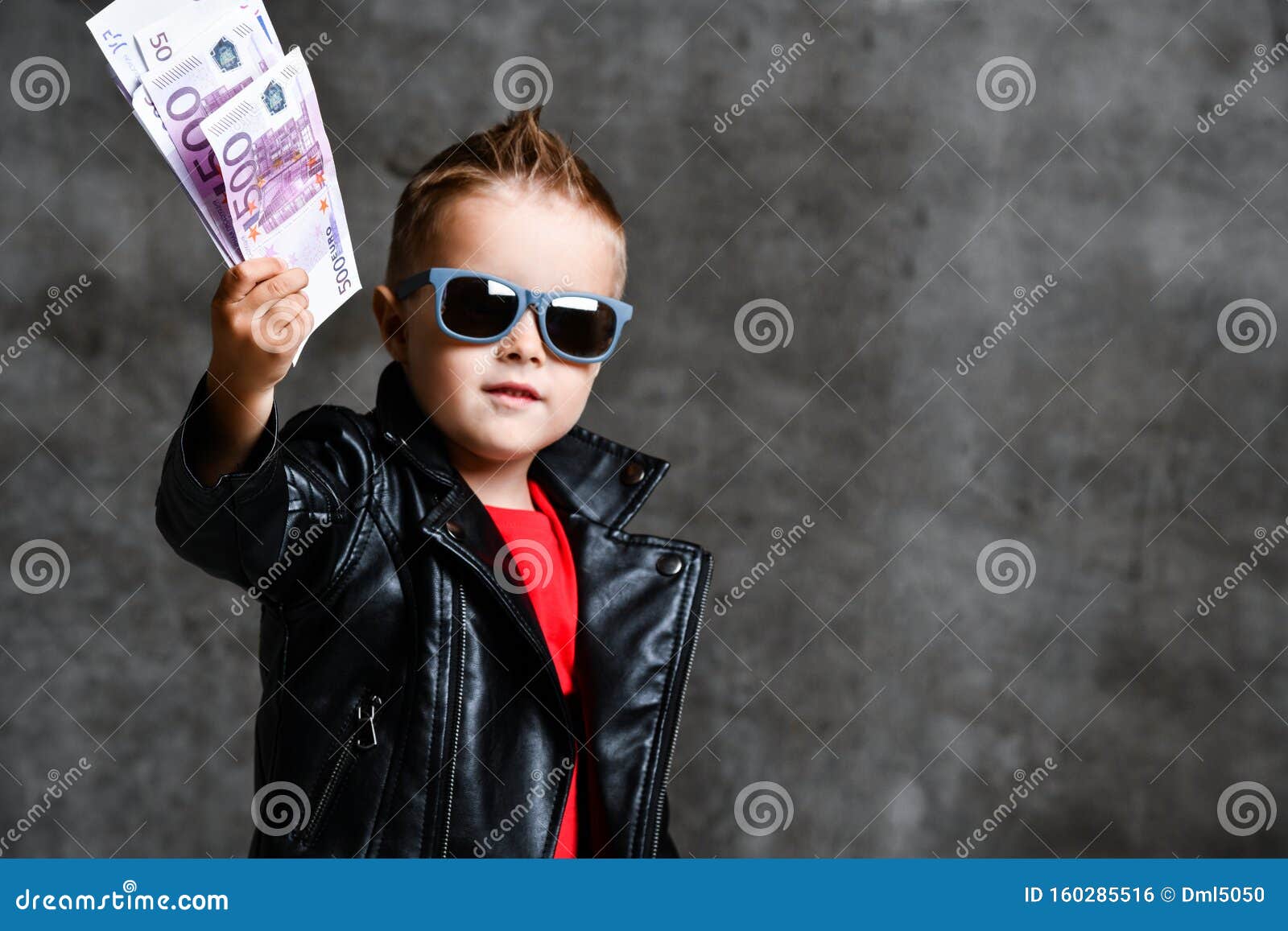 happy rich kid boy millionaire in fashion sunglasses hold stack of 500 euro money cash in leather jacket and red t-shirt