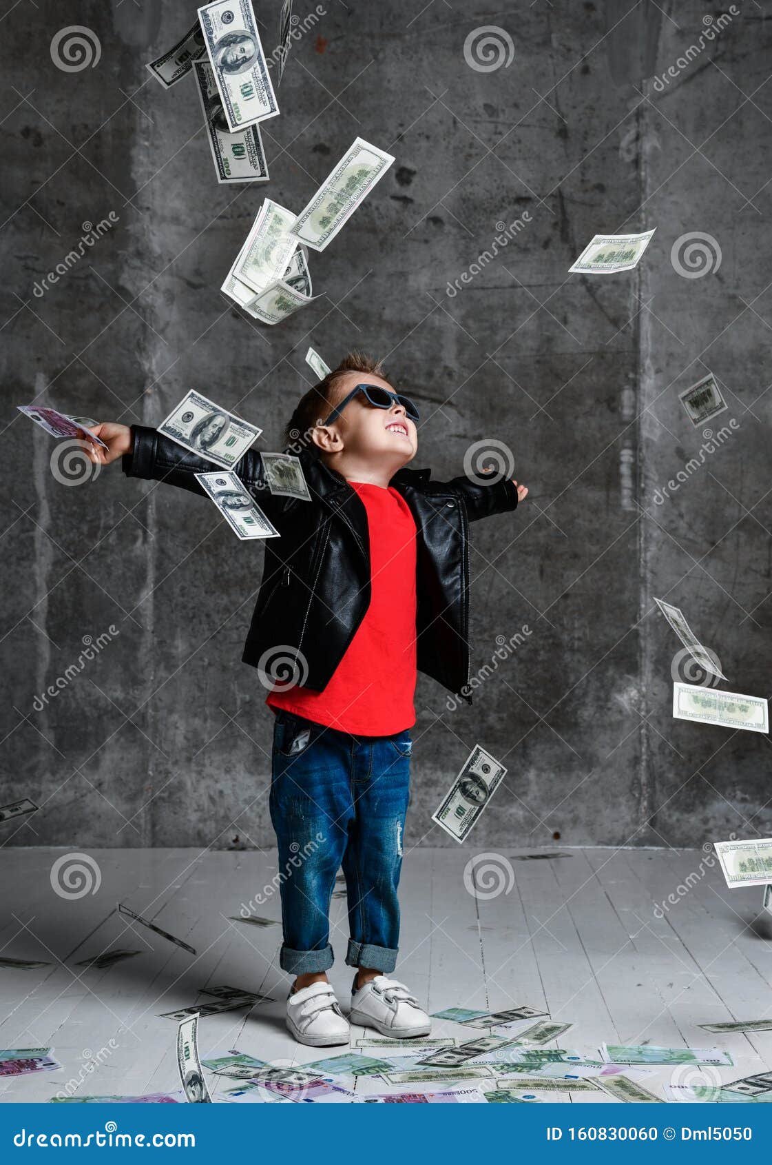 happy rich kid boy in sunglasses, leather jacket and blue jeans is enjoying money rain with wide spread hands