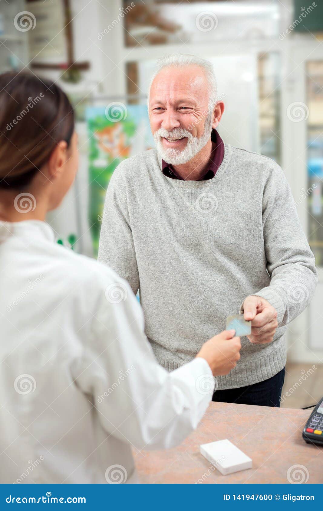 Happy senior man buying medications in a pharmacy, paying with credit card. Happy senior gray haired men buying medications in a pharmacy, paying with credit card. Medicine, pharmaceutics, health care and people concept