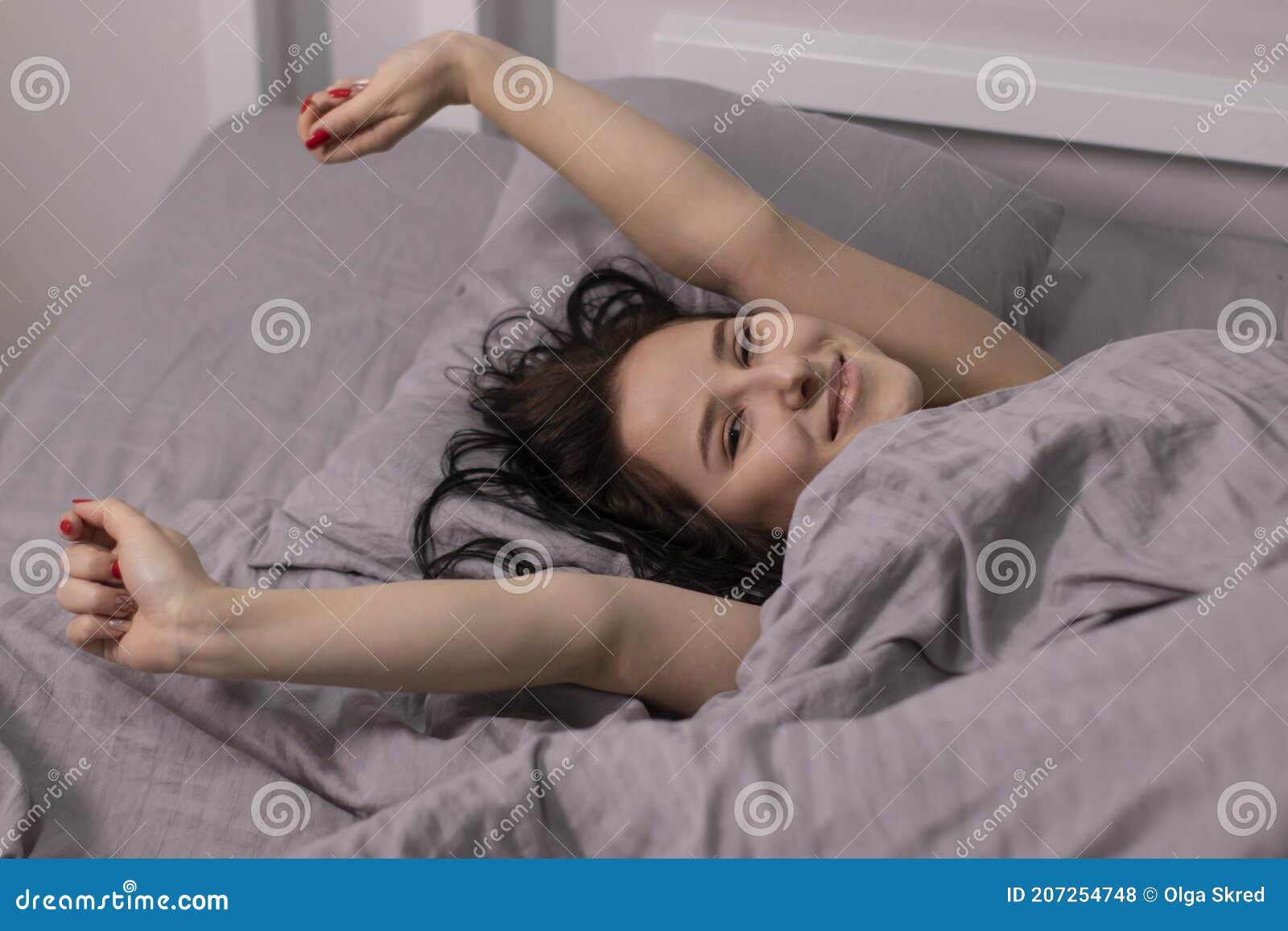 happy sleepy girl brunette in burgundy top under grey sheets in bed. morning routine. good dream, sleeping