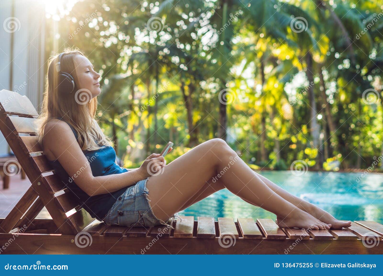Happy Smartphone Woman Relaxing Near Swimming Pool Listening with Earbuds To Streaming Music