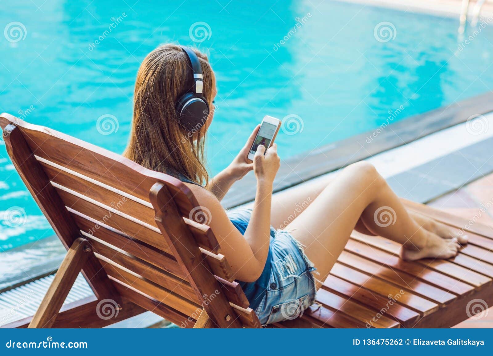 Happy Smartphone Woman Relaxing Near Swimming Pool Listening with Earbuds To Streaming Music