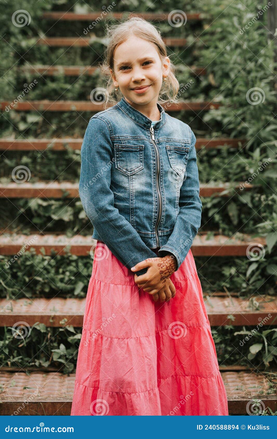 happy smiling candid eight year old kid girl stands on staircase overgrown with grass in nature. prepubertal age of children and t