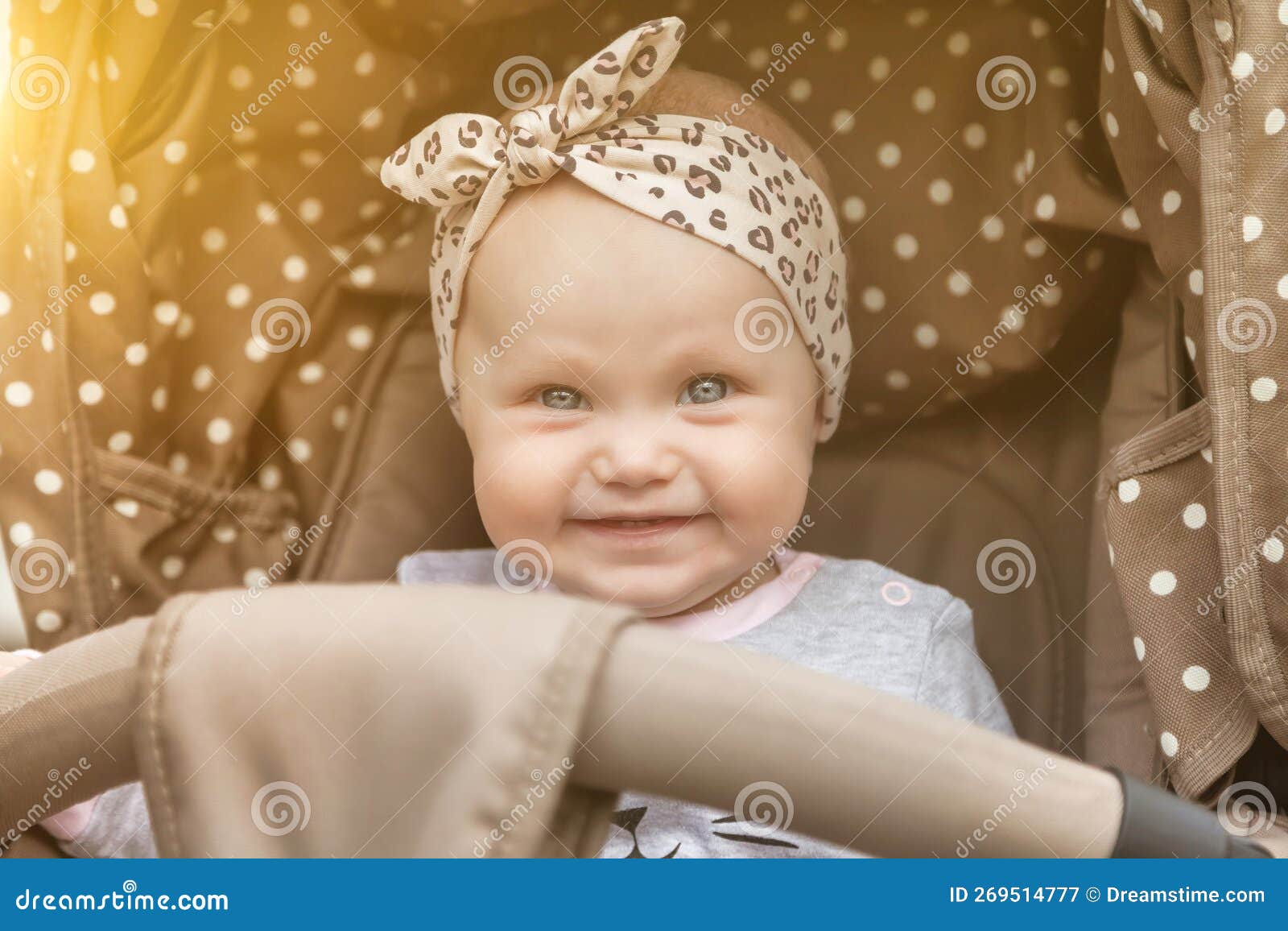 happy smiling emotional eight-month-old blue-eyes girl sitting in stroller looking at camera and wait for parent