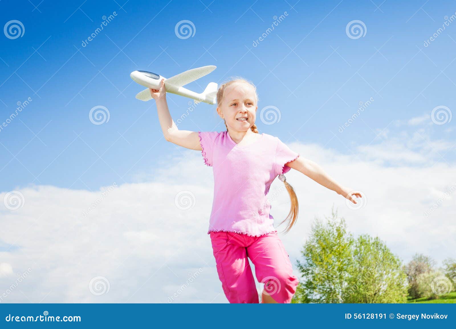 Happy smiling girl holding airplane toy during running in the green filed in summer time