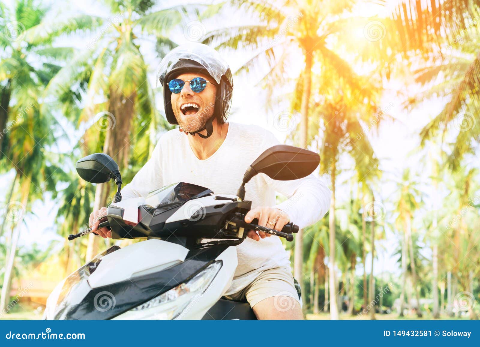 Happy smiling and screaming male tourist in helmet and sunglasses riding motorbike  scooter during his tropical vacation under palm trees Stock Photo - Alamy