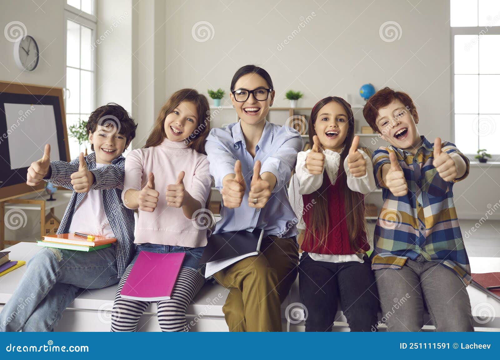 happy smiling teacher with pupils group giving thumbs up portrait in schoolroom