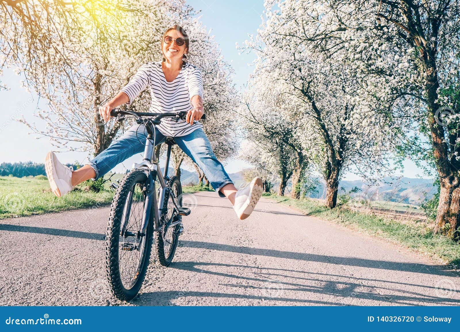 happy smiling woman cheerfully spreads legs on bicycle on the country road under blossom trees. spring is comming concept image