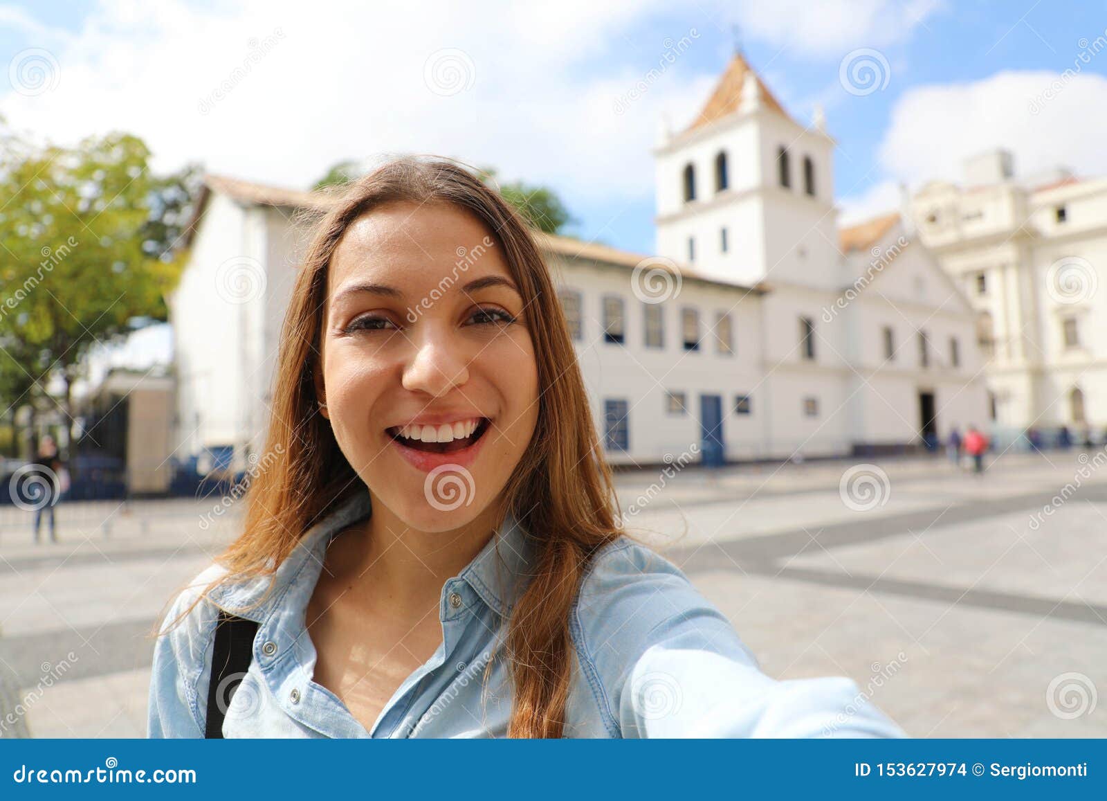 happy smiling young woman in sao paulo city center take self portrait with patio do colegio landmark on the background, sao paulo