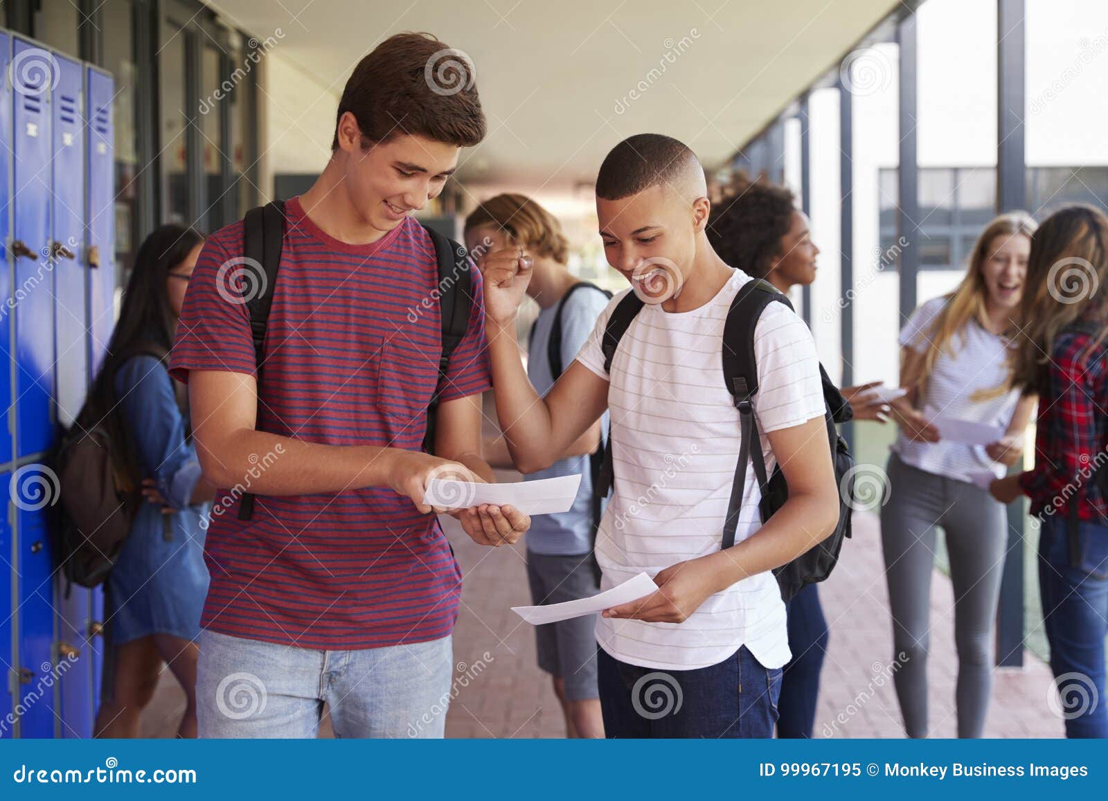 happy teenage boys sharing exam results in school corridor