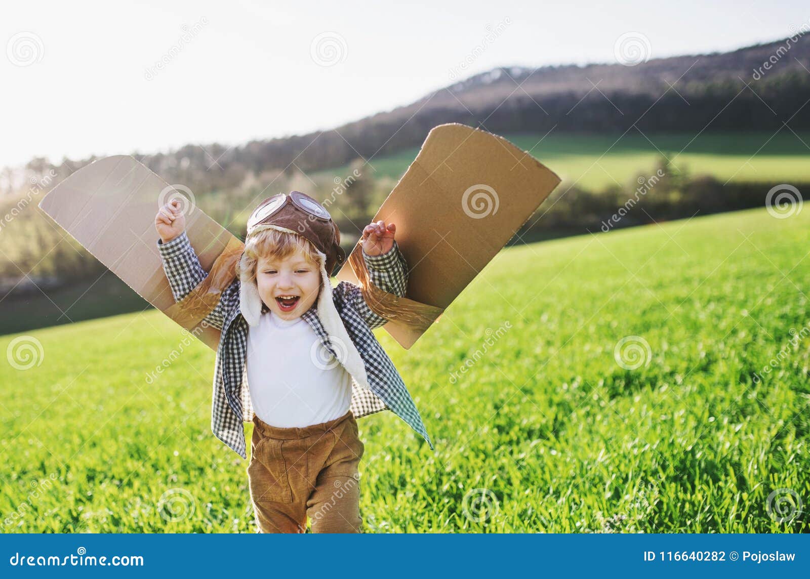 happy toddler boy with wings playing outside in spring nature.