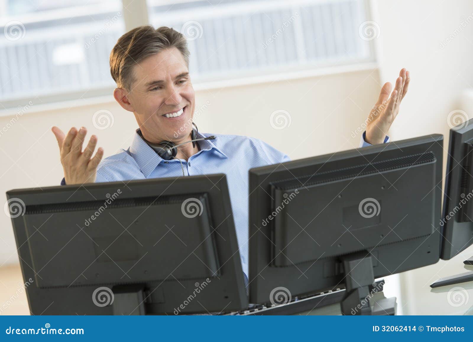 happy trader gesturing while using multiple screens at desk