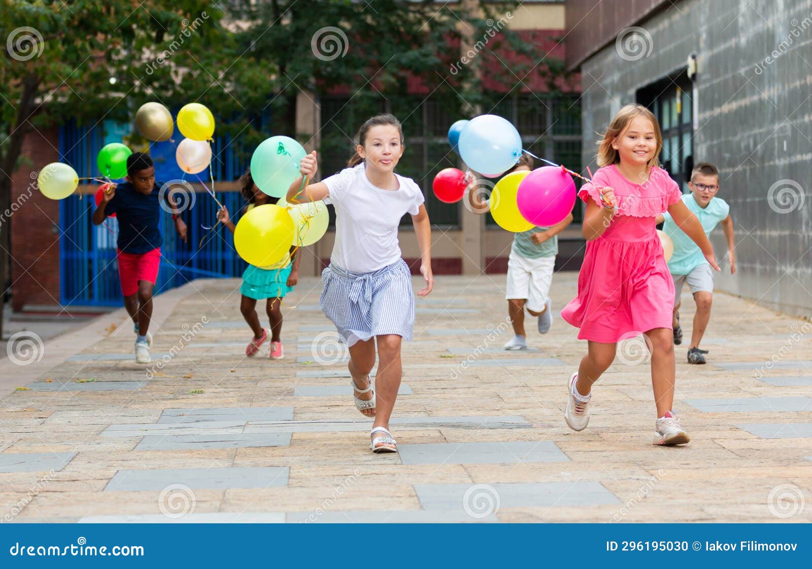 Happy Tweens Wth Colorful Balloons Chasing Each Other On City Street