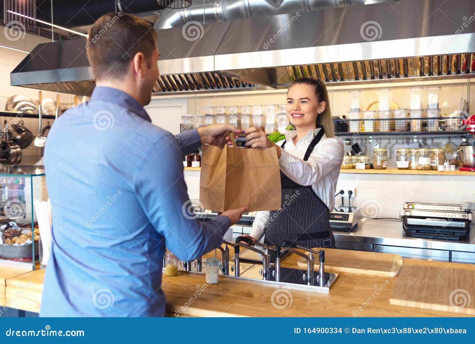 happy waitress waring apron serving customer at counter in small family eatery restaurant