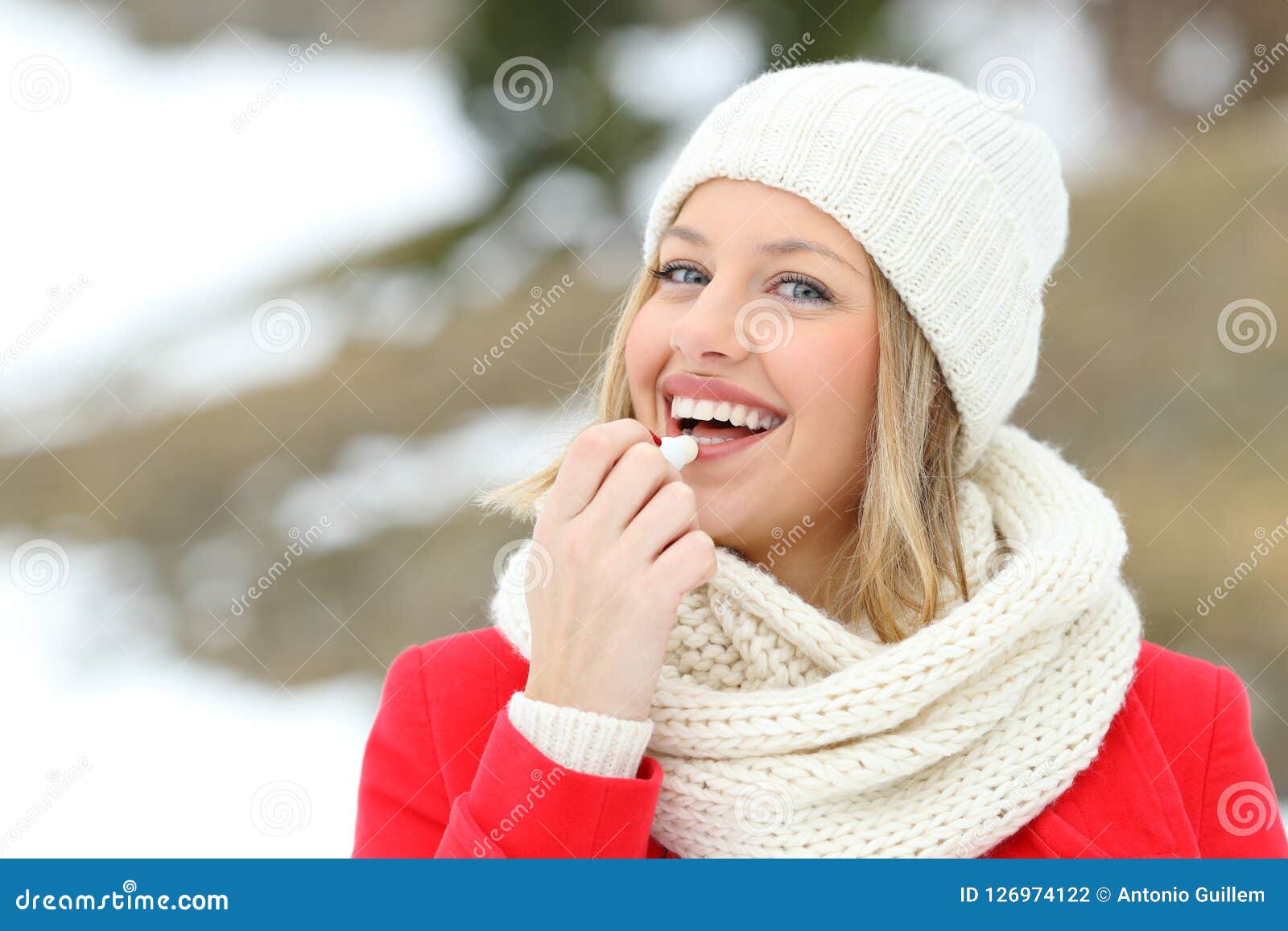 happy woman applying lip balm outdoors in winter