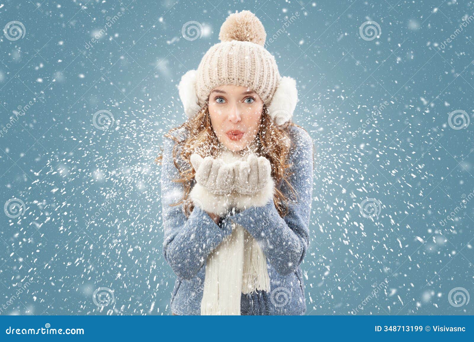 happy woman blowing snow from her hands looking into the camera,  in snowfall on blue background. the christmas holidays