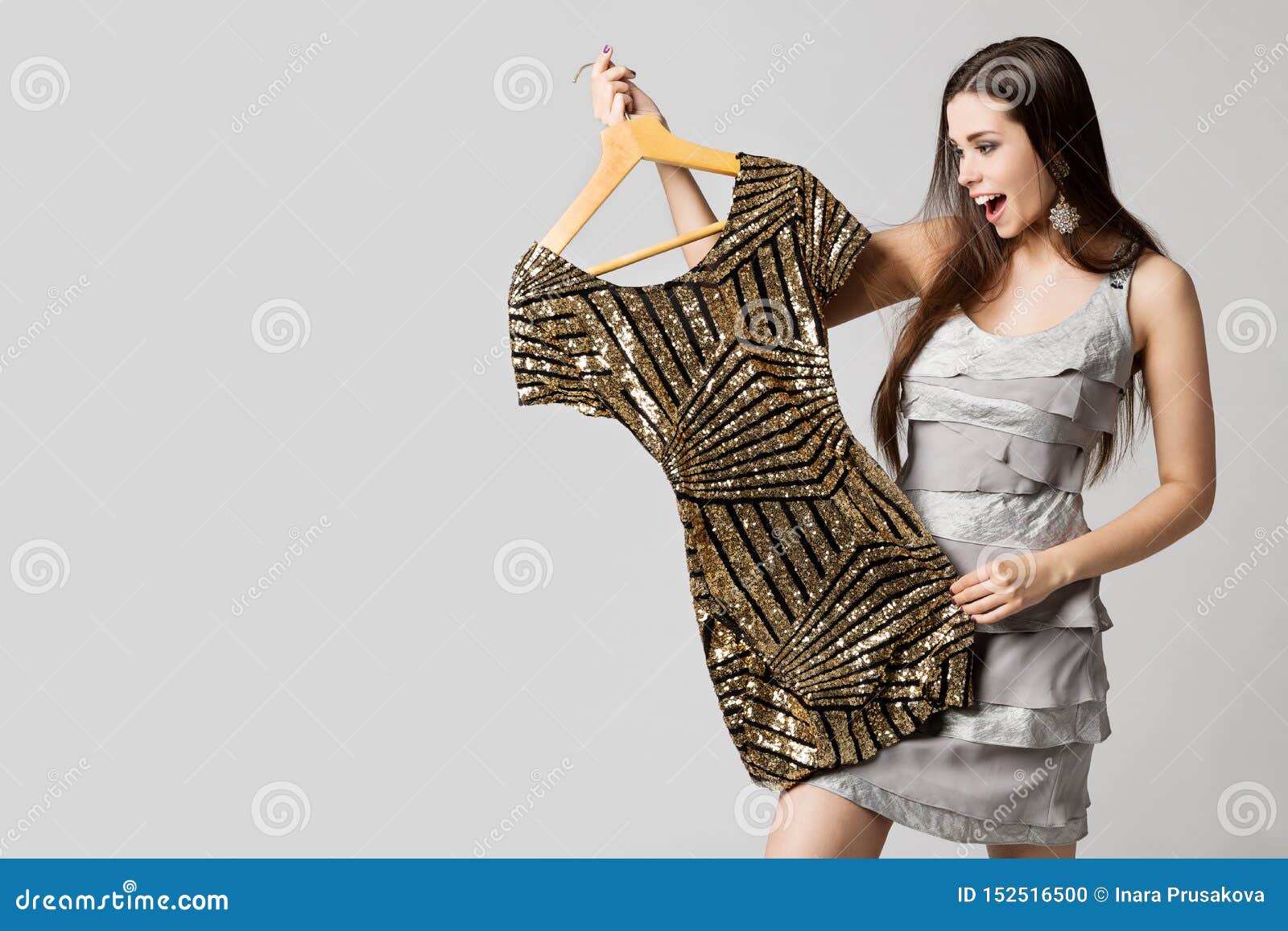 happy woman choosing dress, attractive girl holding gold clothes on hanger on white