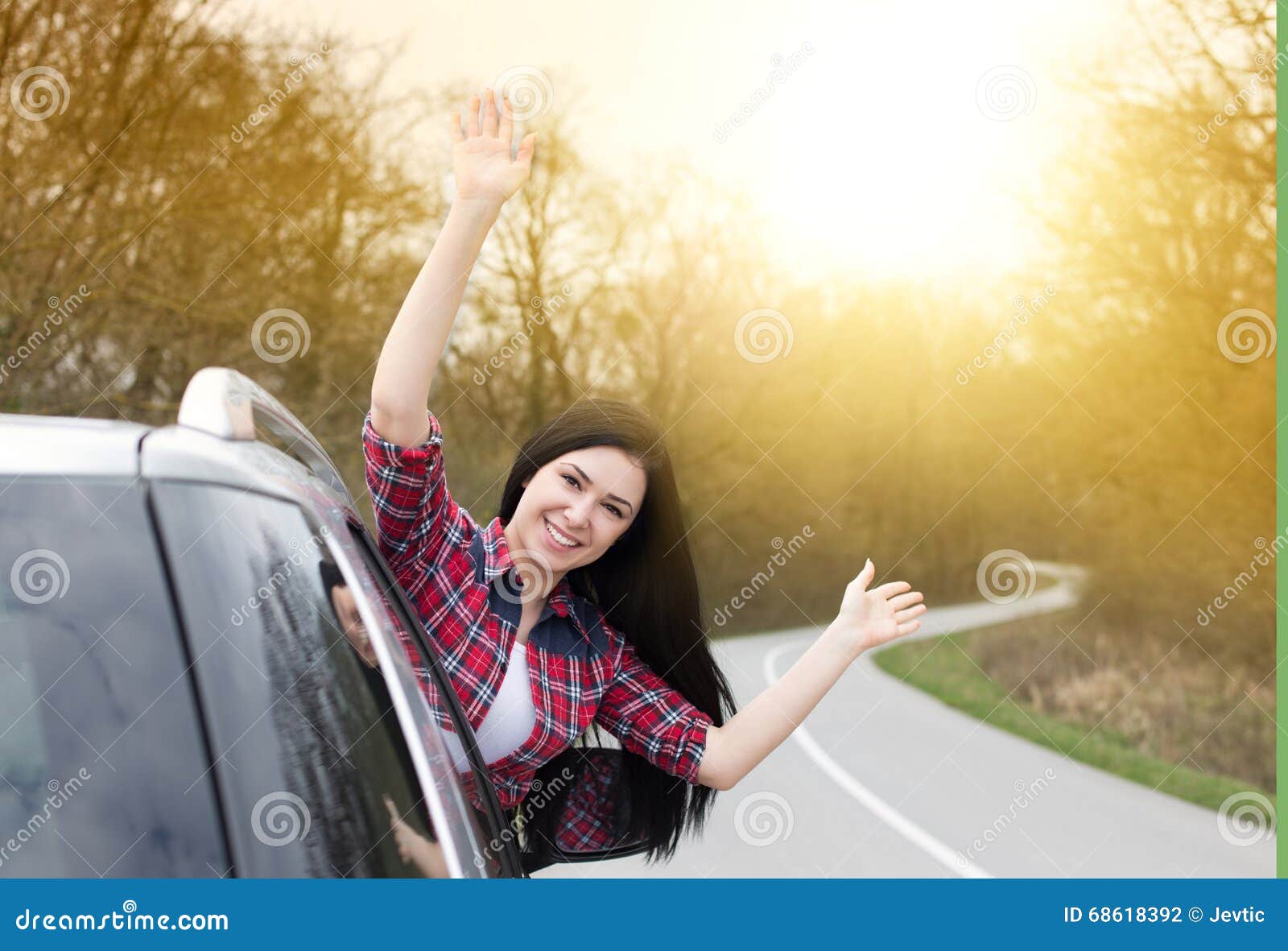 Happy woman looking out of the car. Happy young woman with raised arms looking out of car on the road