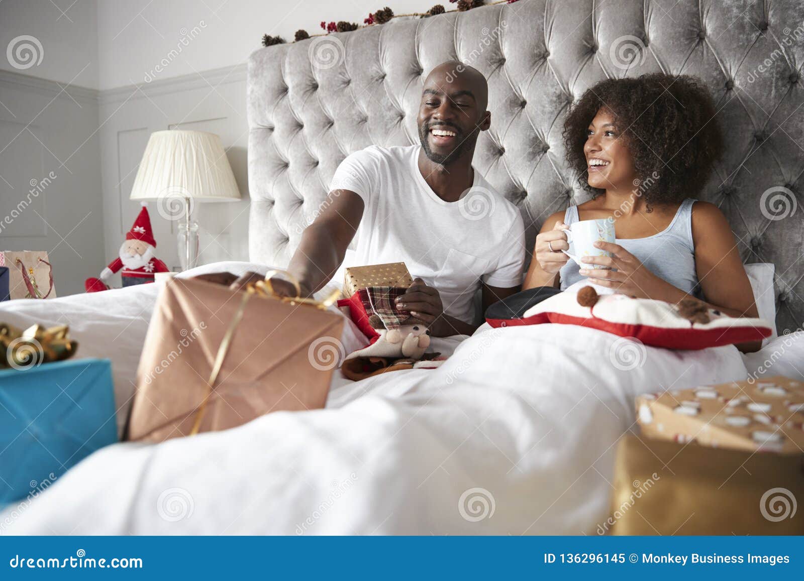 Happy Young Black Couple Sitting in Bed Giving Gifts To Each Other on ...