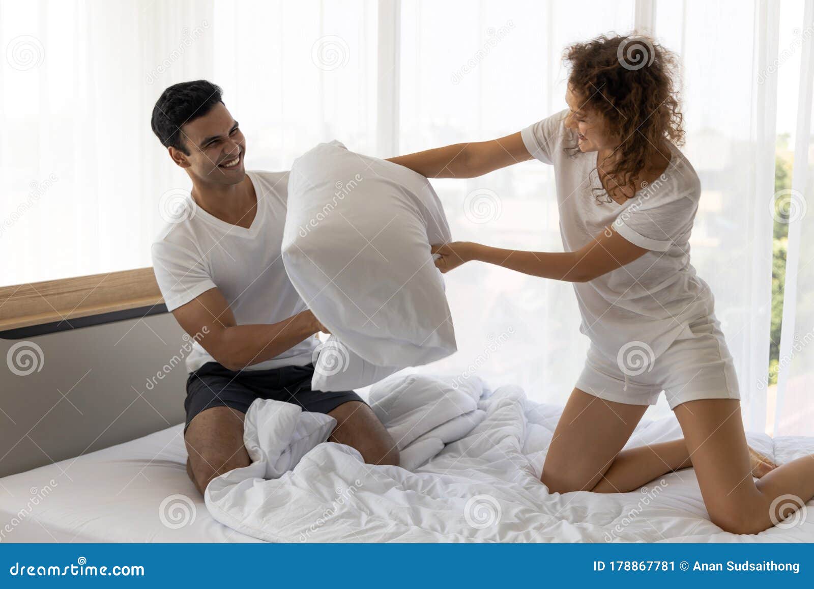 Happy Young Couple Having Fun With Pillow Fight On The Bed In Bedroom