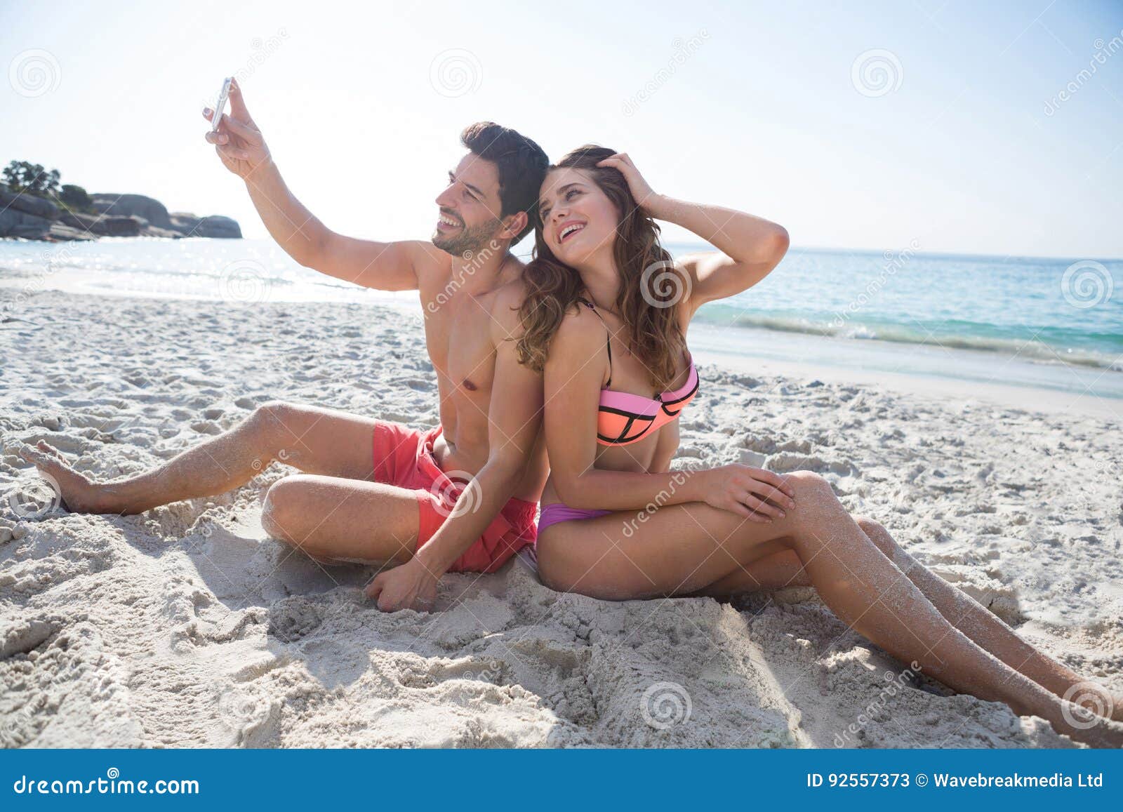 happy young couple taking selfie while sitting at beach