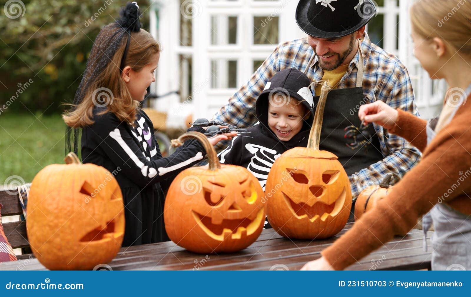 happy young family in halloween costumes carving pumpkins together in backyard