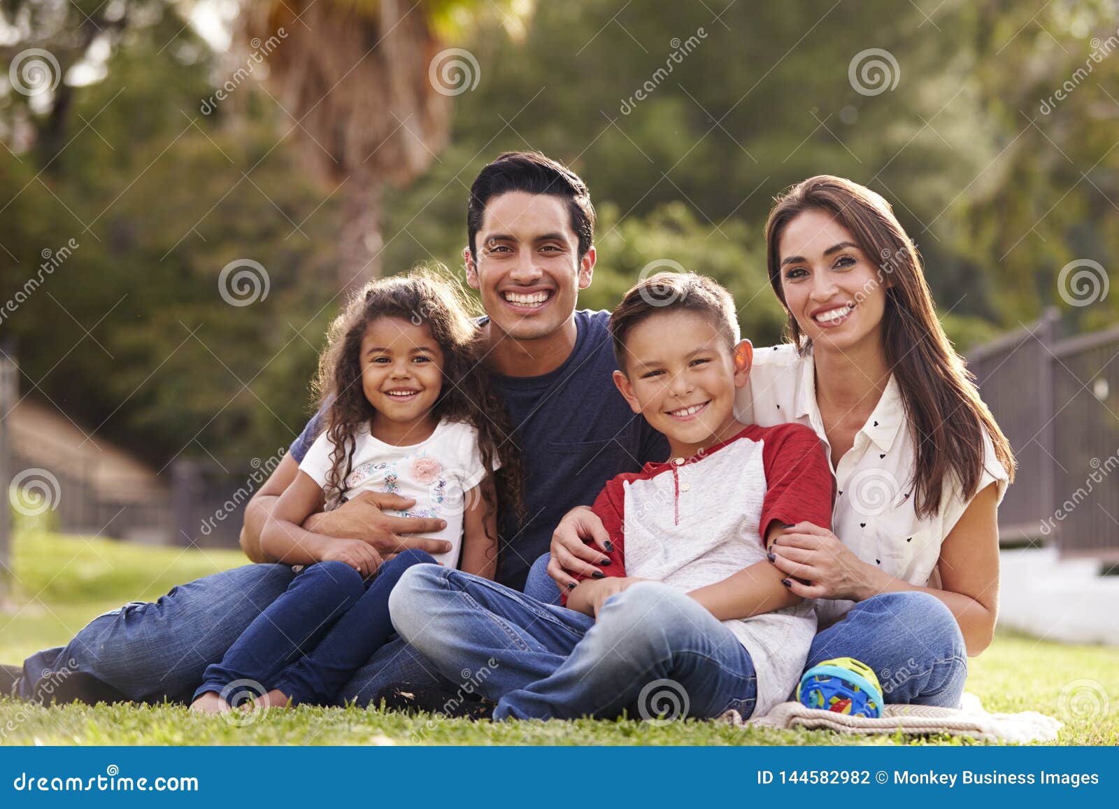 happy young hispanic family sitting the on grass in the park smiling to camera, close up
